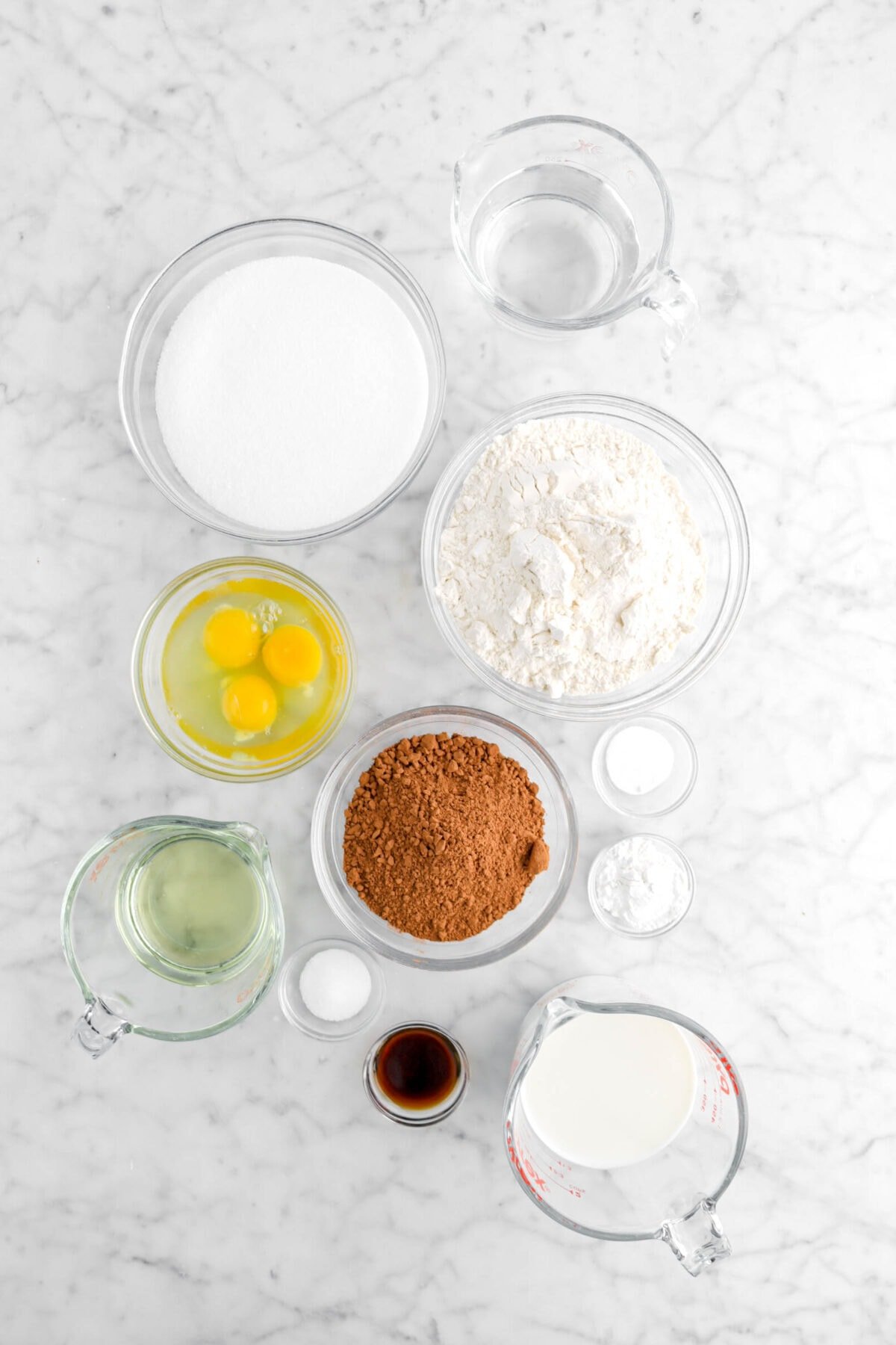 water, sugar, flour, eggs, cocoa powder, baking soda, baking powder, milk, vanilla, salt, and oil on marble surface