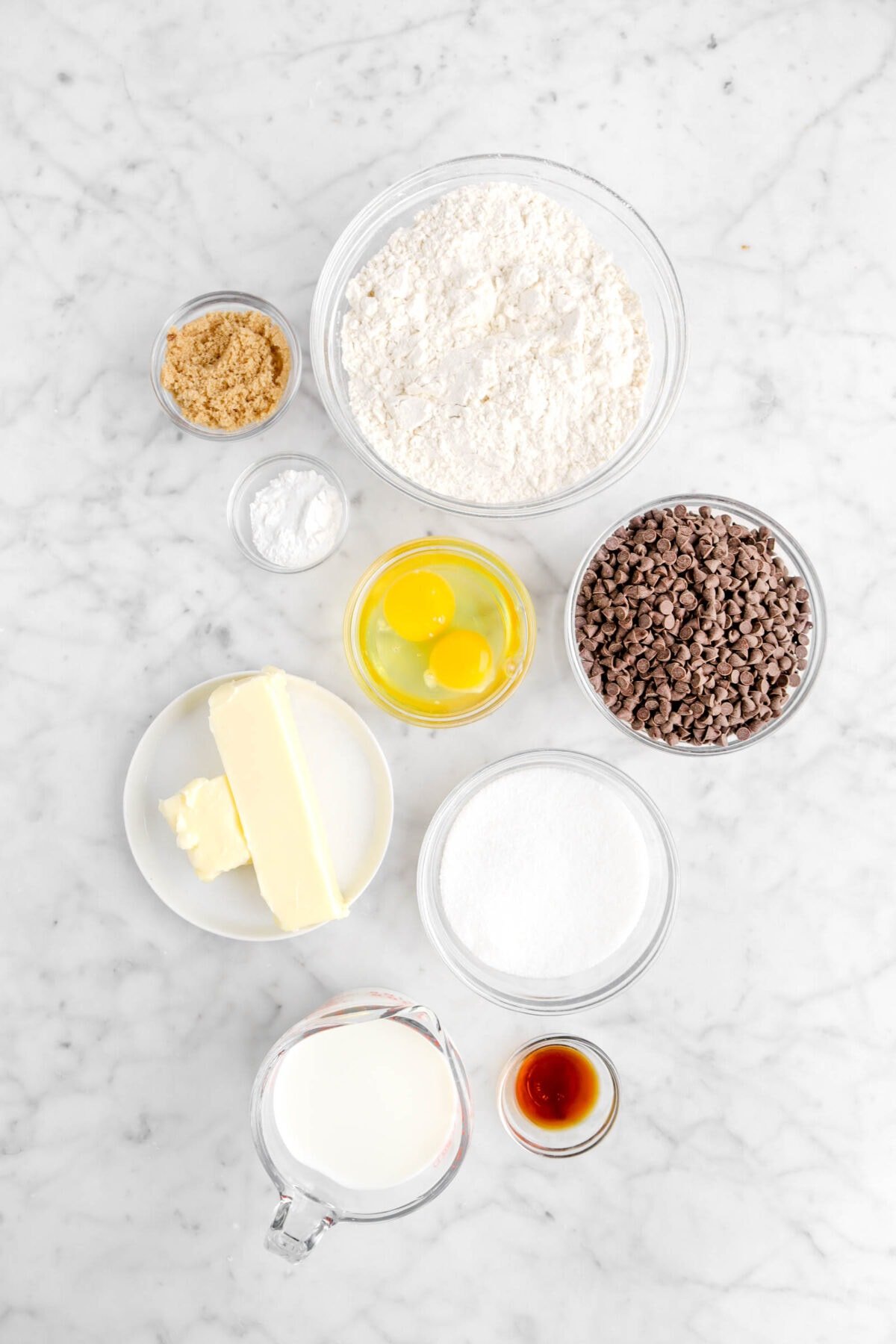 brown sugar, baking powder, flour, eggs, mini chocolate chips, sugar, butter, vanilla, and milk on marble counter