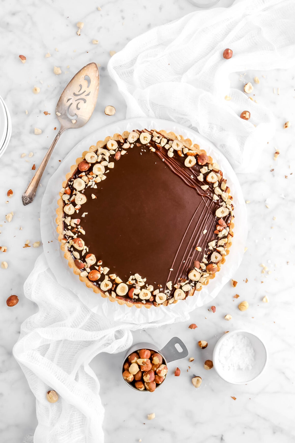 chocolate hazelnut tart with chocolate drizzle and hazelnuts on top with cake knife and white cheese cloth