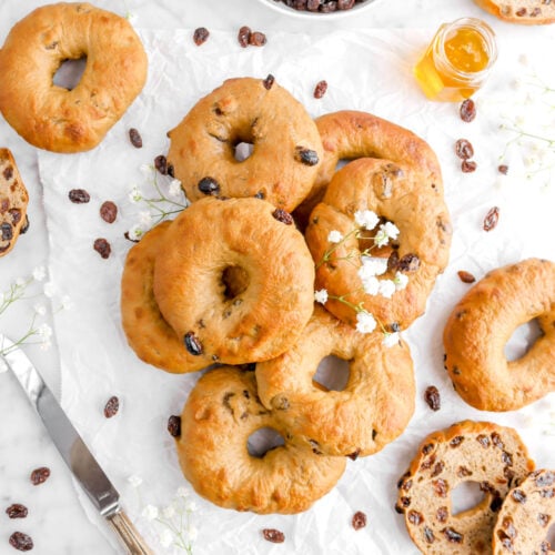 piled cinnamon raisin bagels on parchment paper with more ariound