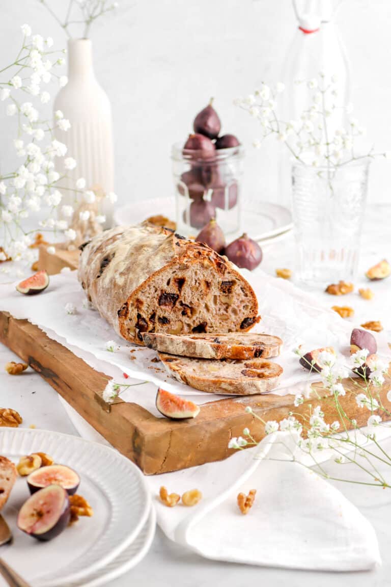fig and walnut bread with two slices laying in front and flowers around with fresh figs and walnuts around