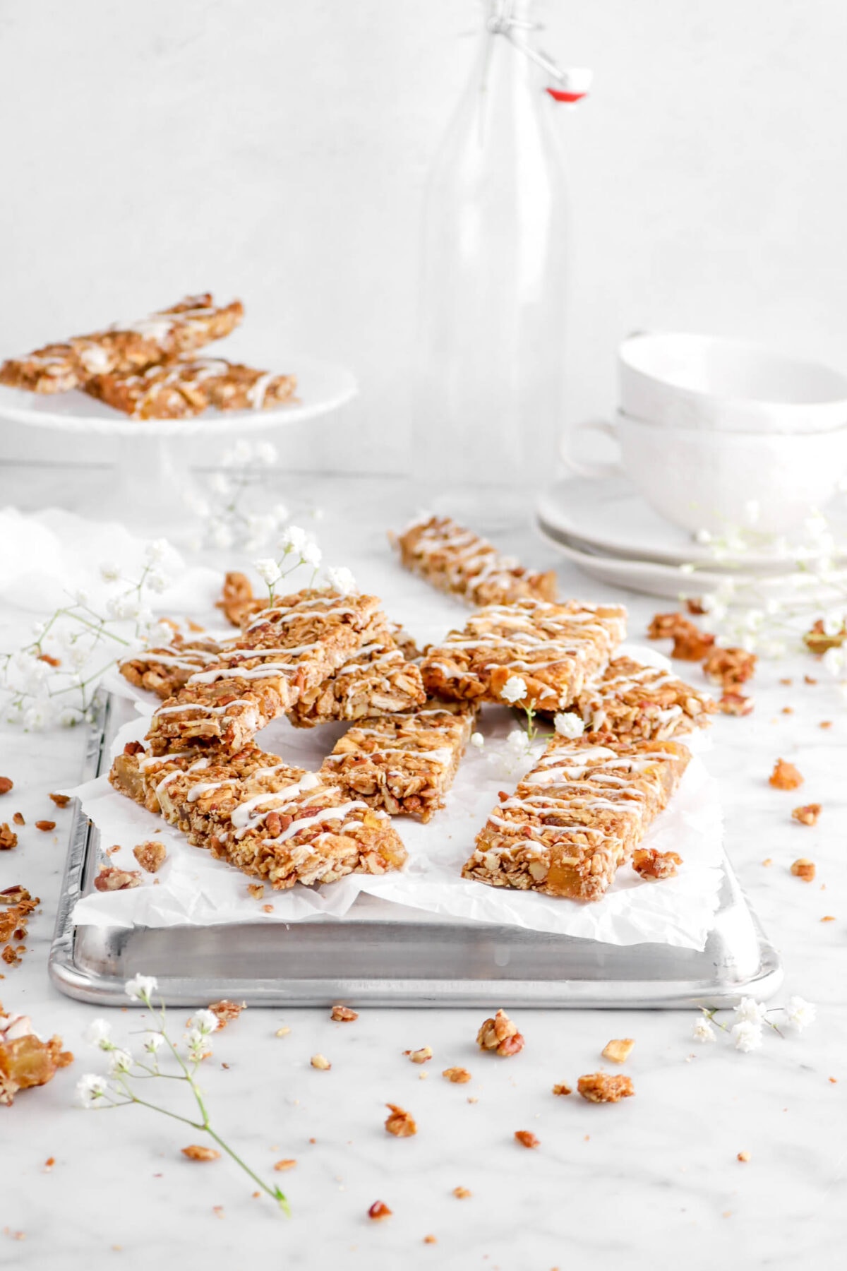 hummingbird granola bars on sheet pan with parchment paper, flowers, plates, and mugs behind