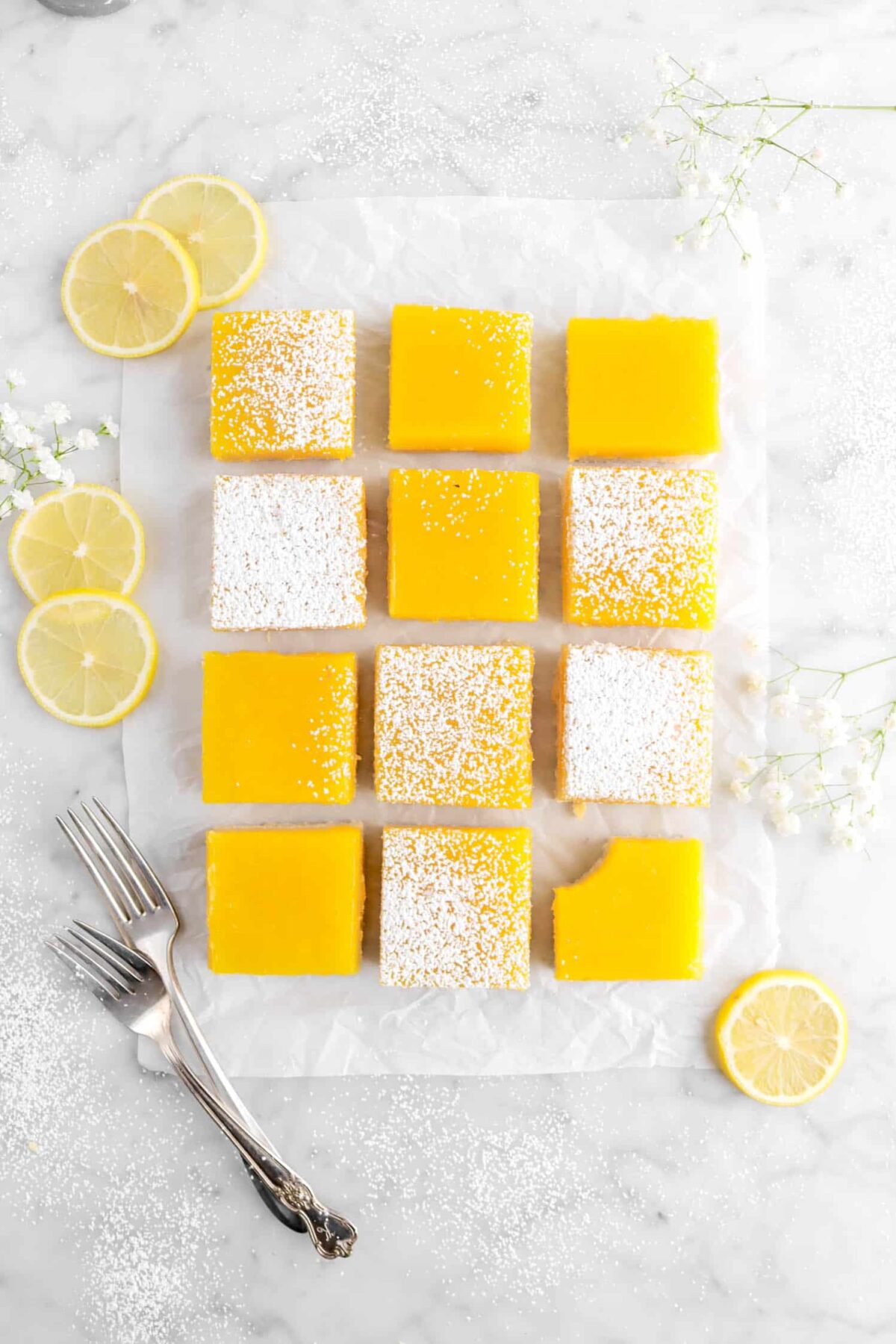 overhead photo of twelve lemon bars on parchment paper with a bite taken out of one