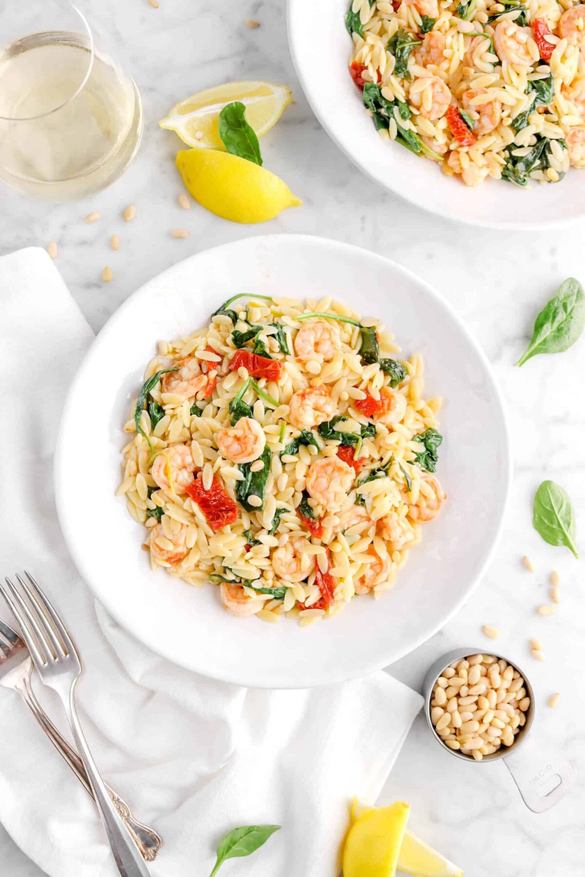 shrimp orzo in plate with forks, spinach leaves, pine nuts, and lemon wedges around