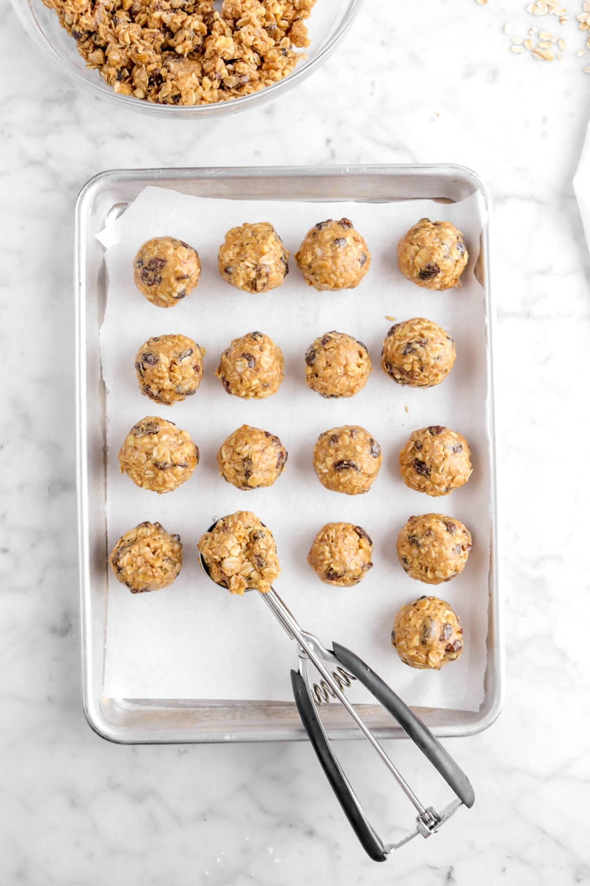16 energy bites on lined sheet pan with cookie scoop full of dough and bowl of dough