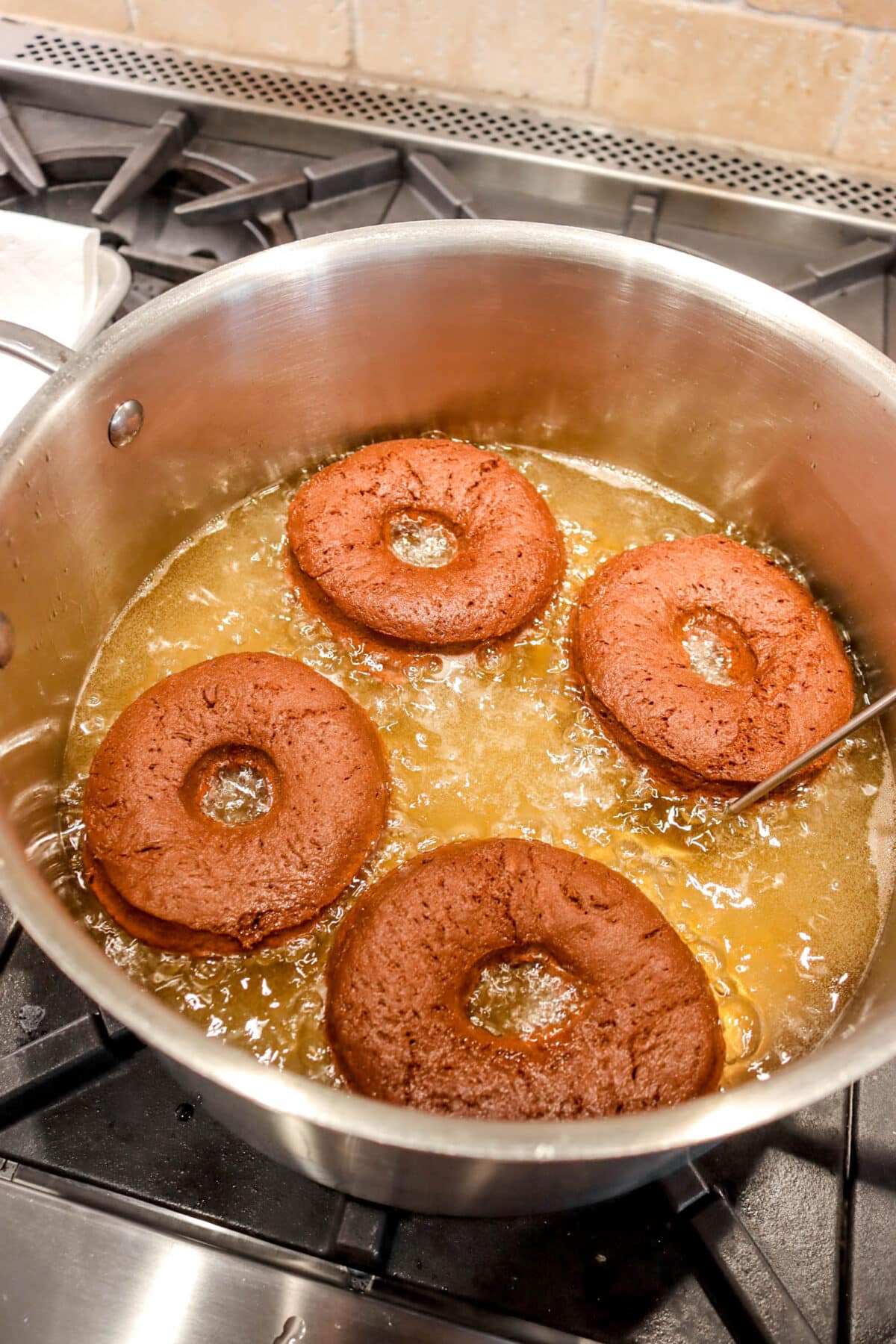 four chocolate doughnuts frying in oil