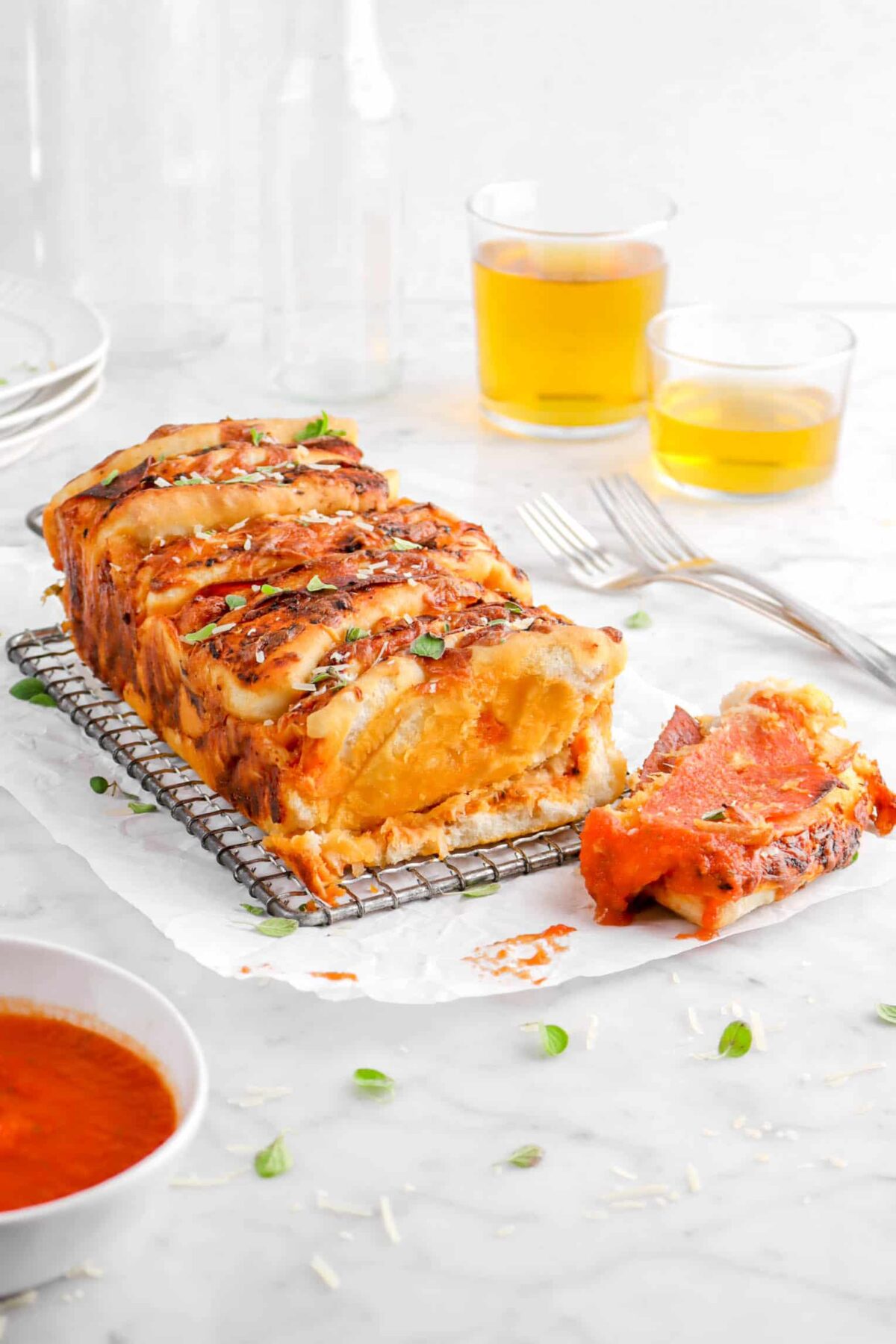 pizza bread on wire cooling rack with two glasses of beer behind, two forks, and slice that has been dipped in tomato sauce in front
