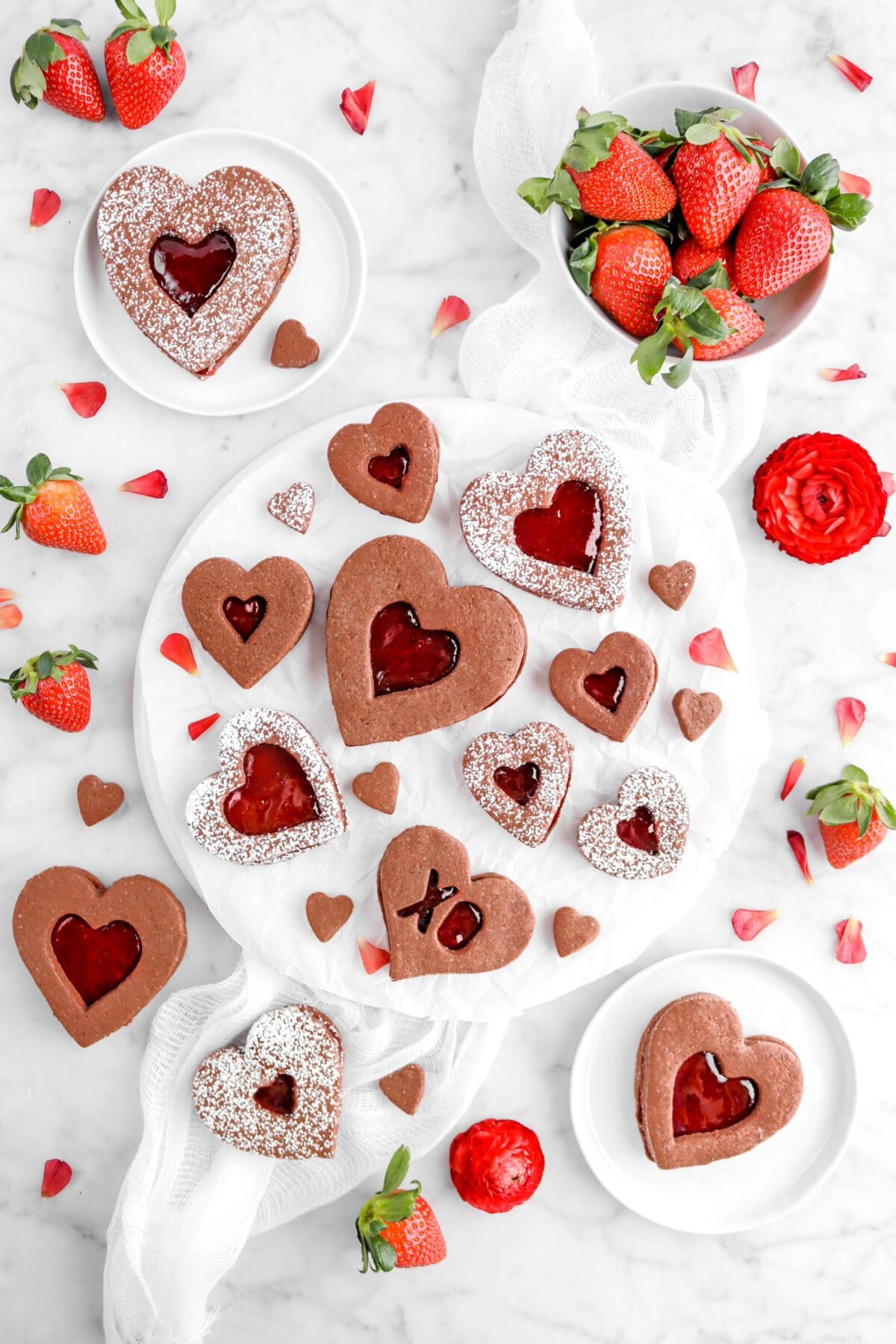 overhead shot of heart shaped chocolate linzer cookies with strawberries and red flowers