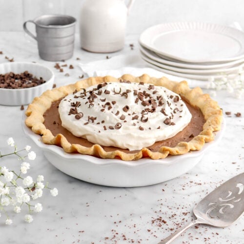 french silk pie with flowers, chocolate curls, and stack of plates on marble surface