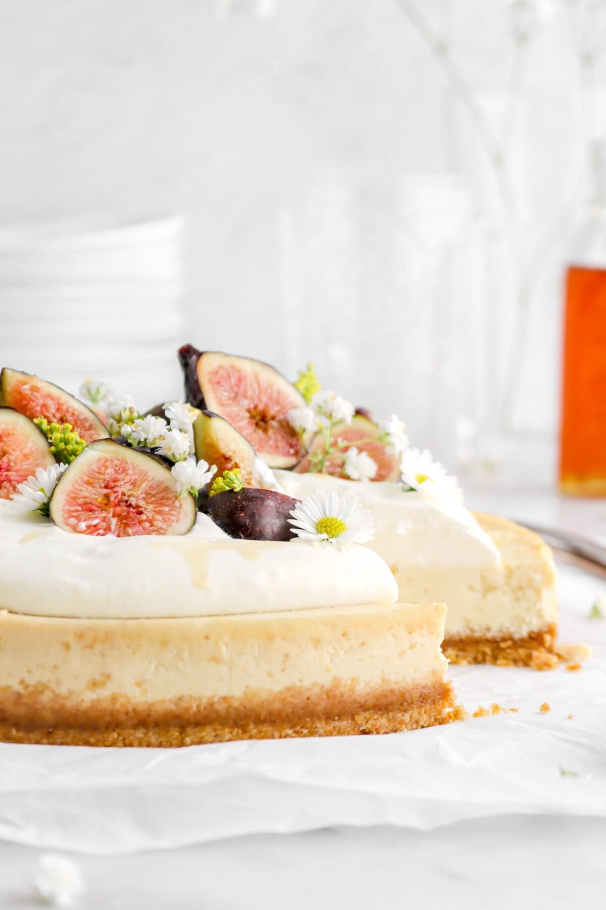close up of honey and goat cheese cheesecake with whipped cream, fresh figs, and flowers with slice missing