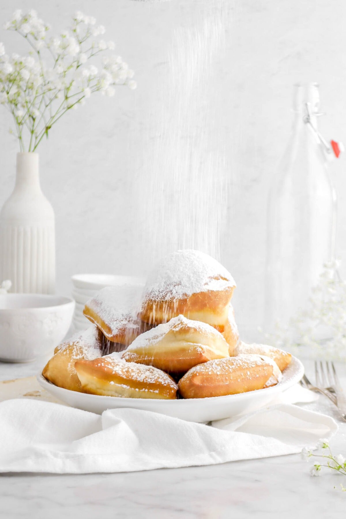 beignets in white bowl with powdered sugar dusting the tops with white napkin
