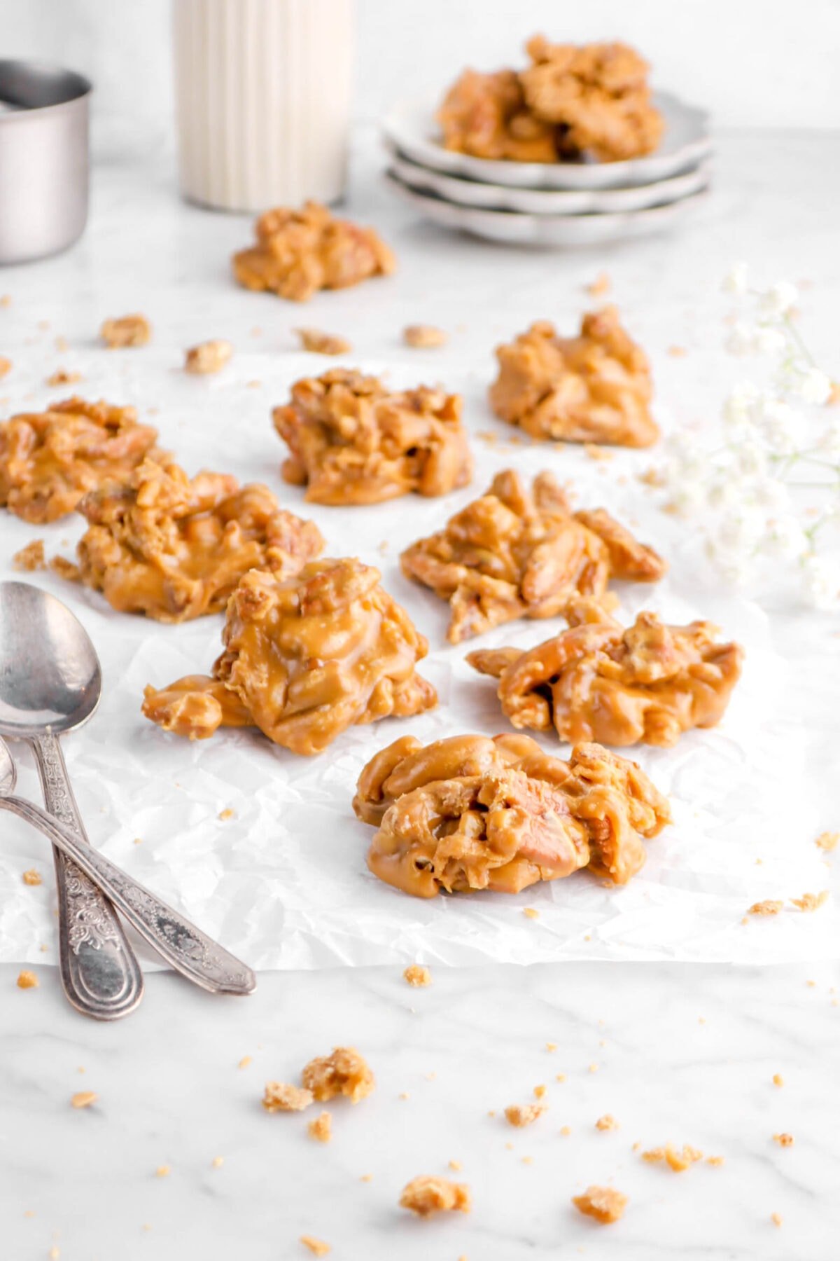 pecan pralines on parchment paper with two spoons and flowers behind