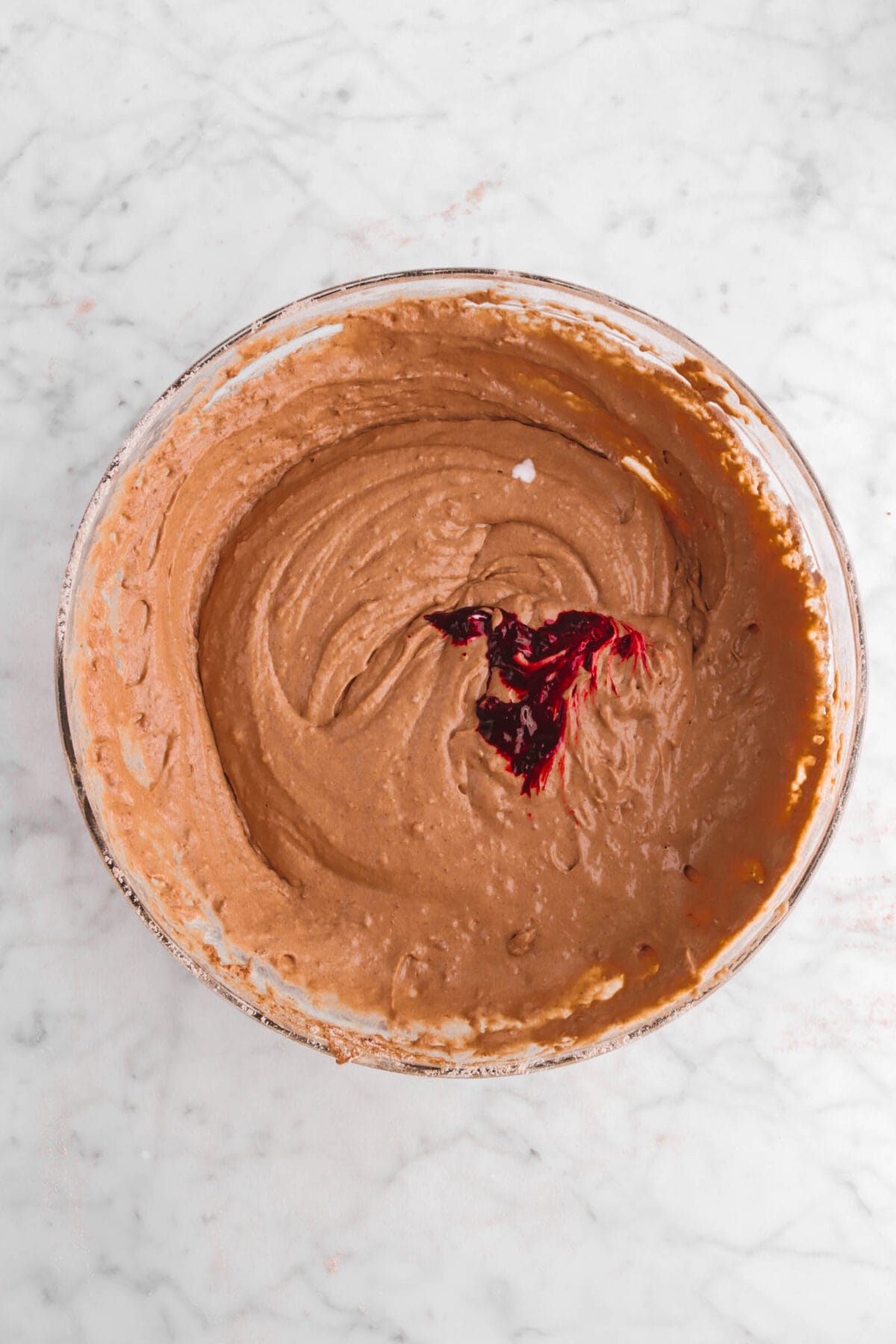 red food dye added to chocolate batter in glass bowl