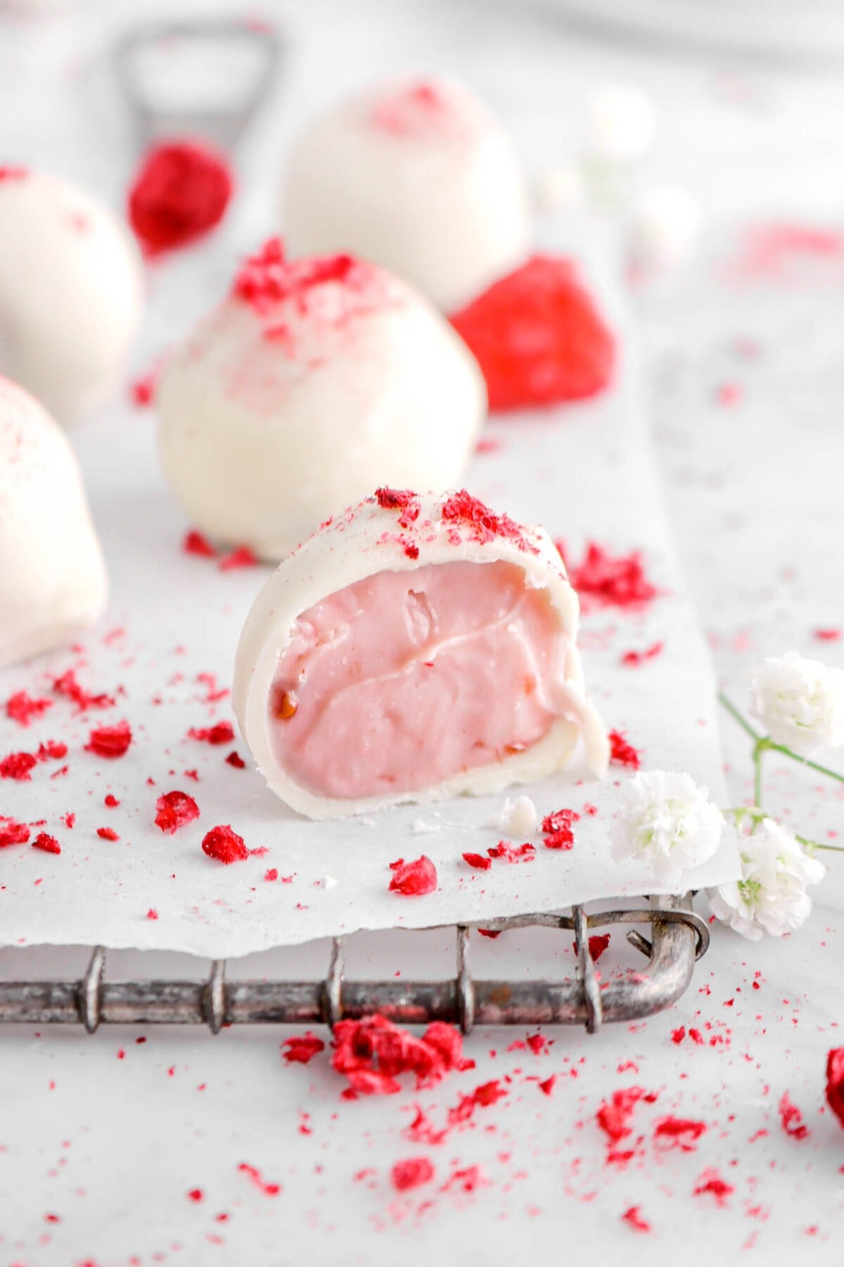 close up photo of cut open raspberry white chocolate truffle with more truffles behind