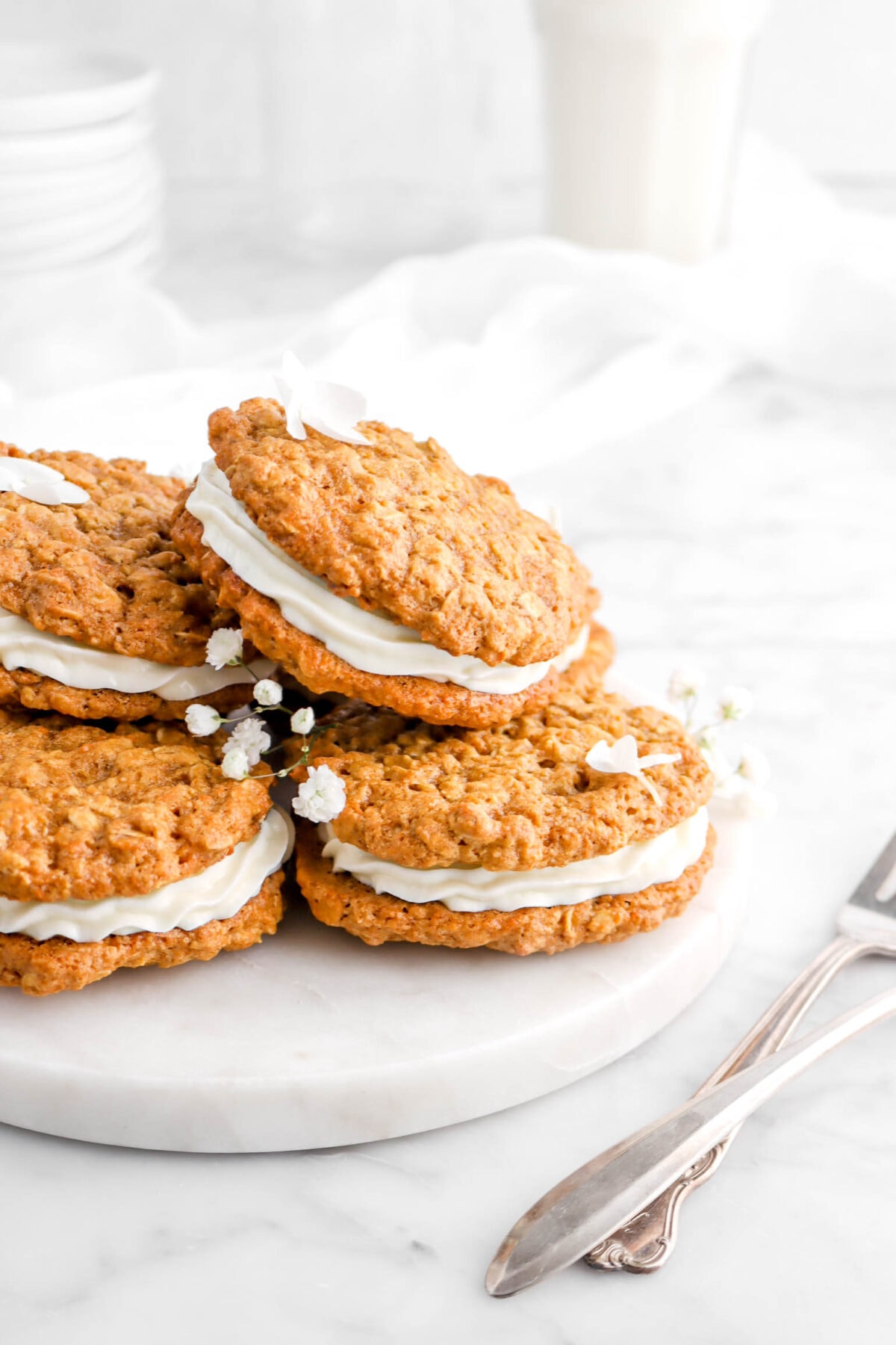 angled close up of stacked carrot cake sandwich cookies on marble surface with white flowers on top and forks beside