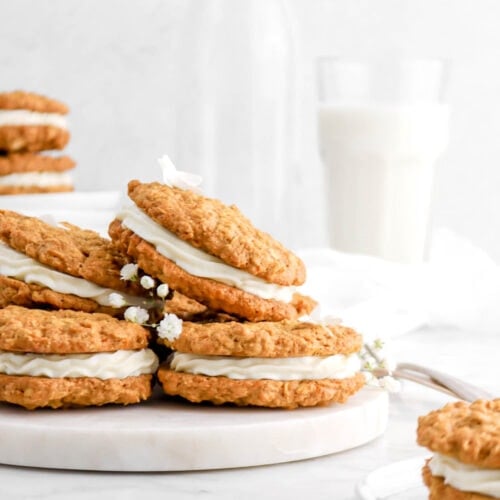 close front shot of stacked carrot cake sandwich cookies with sandwich cookies in front and behind with white flowers and glass of milk