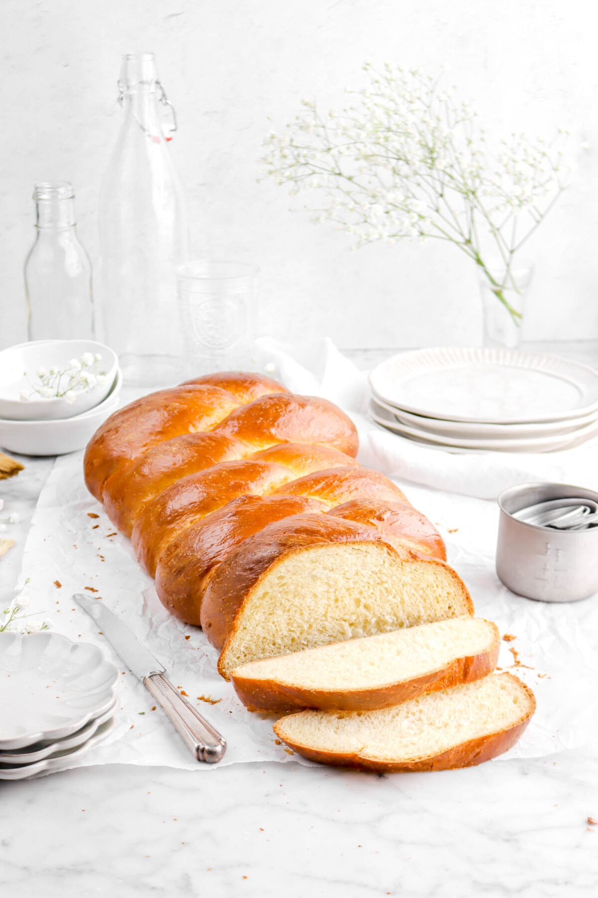 challah with two slices laying in front, flowers, plates, bowls, and empty glasses behind