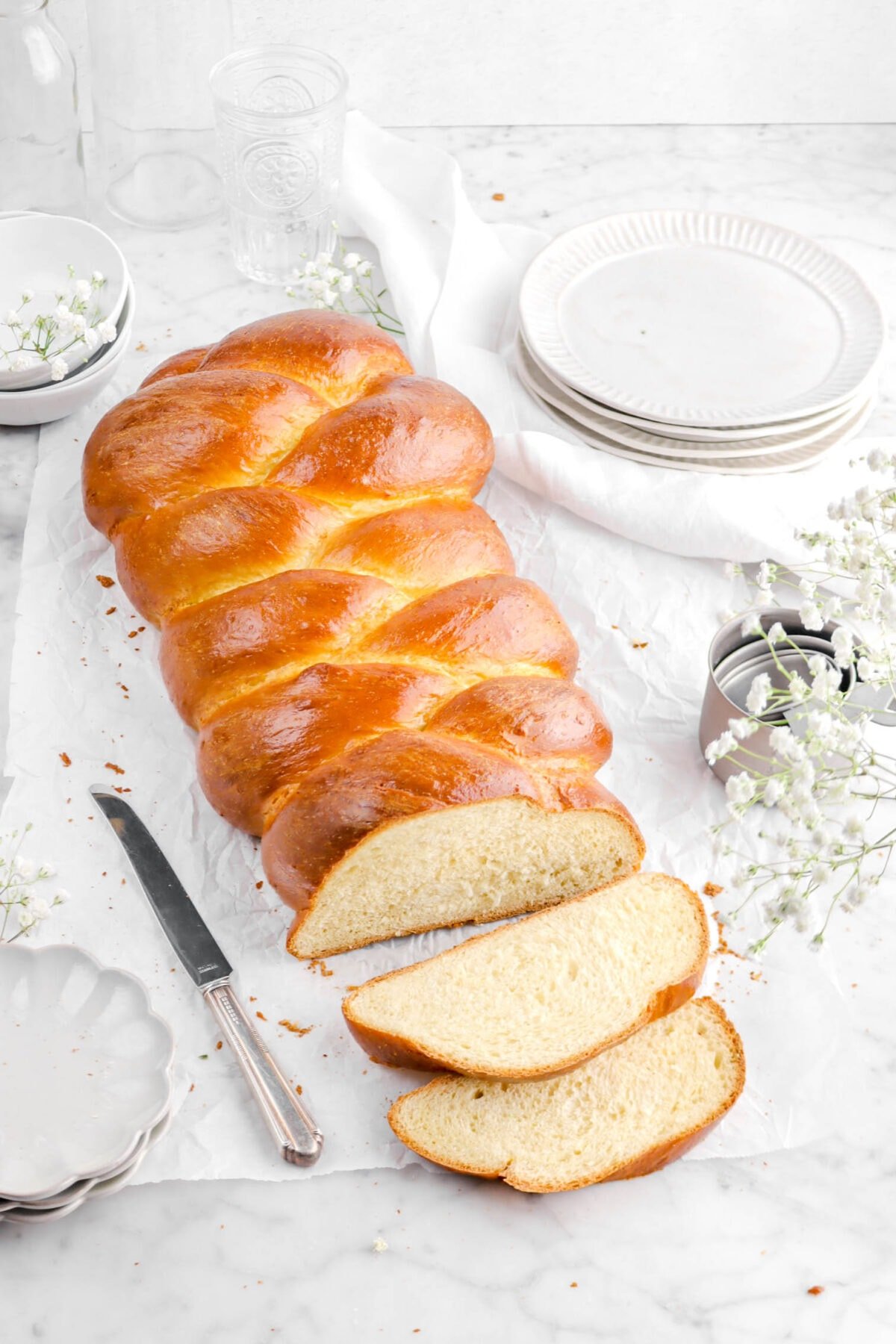 angled shot of challah with two slices laying in front with plates, flowers, and a knife