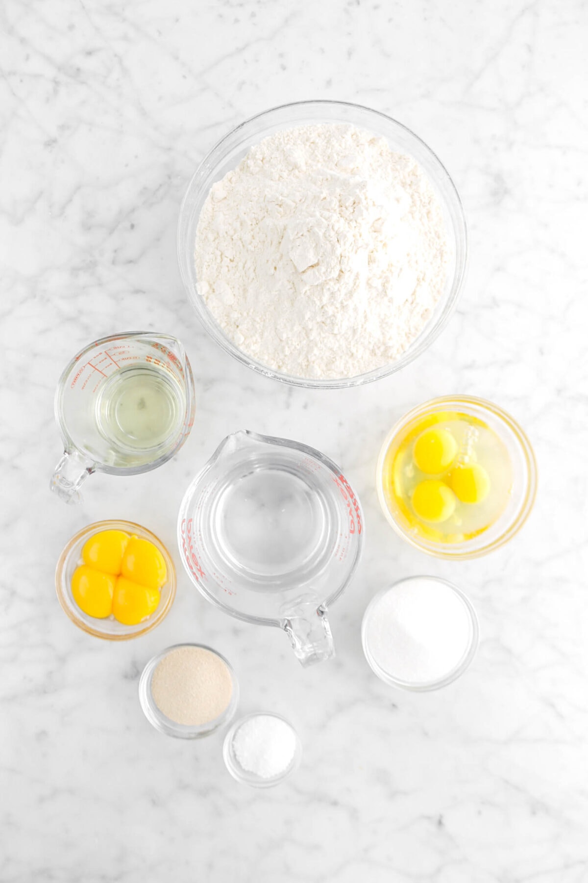 flour, oil eggs, water, egg yolks, yeast, salt, and sugar on marble surface