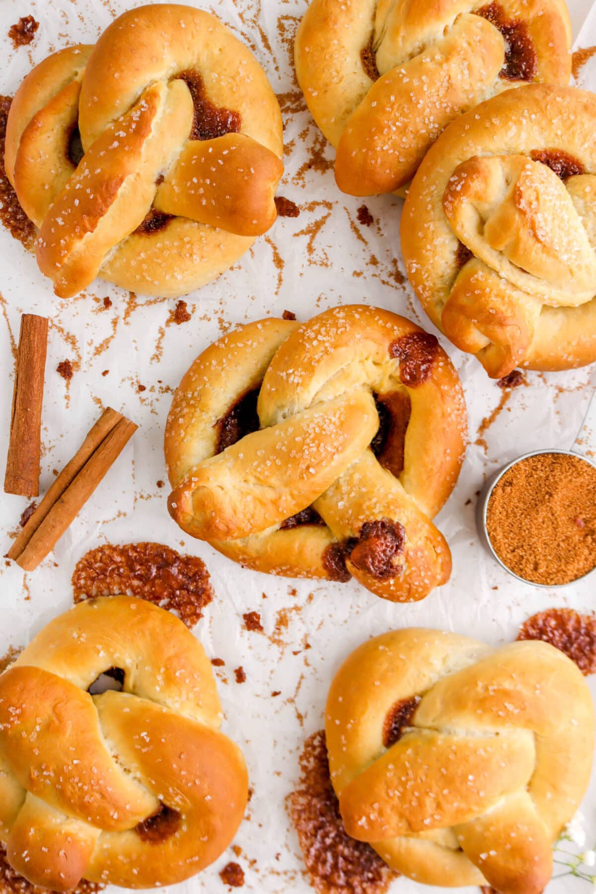 close up of pretzels on parchment paper with cinnamon sugar and cinnamon sticks around