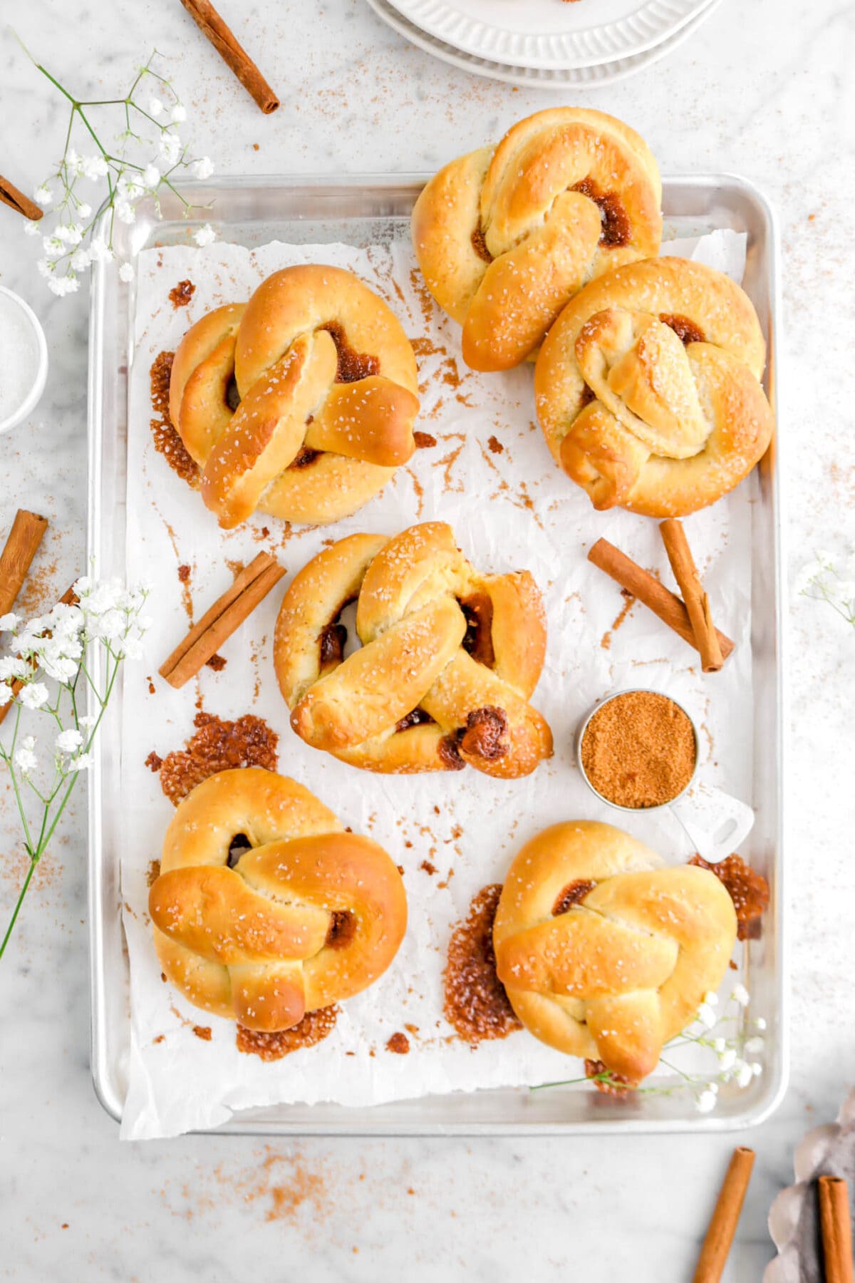 overhead shot of pretzels on lined sheet pan with flowers and cinnamon sticks and a bite missing from middle pretzel