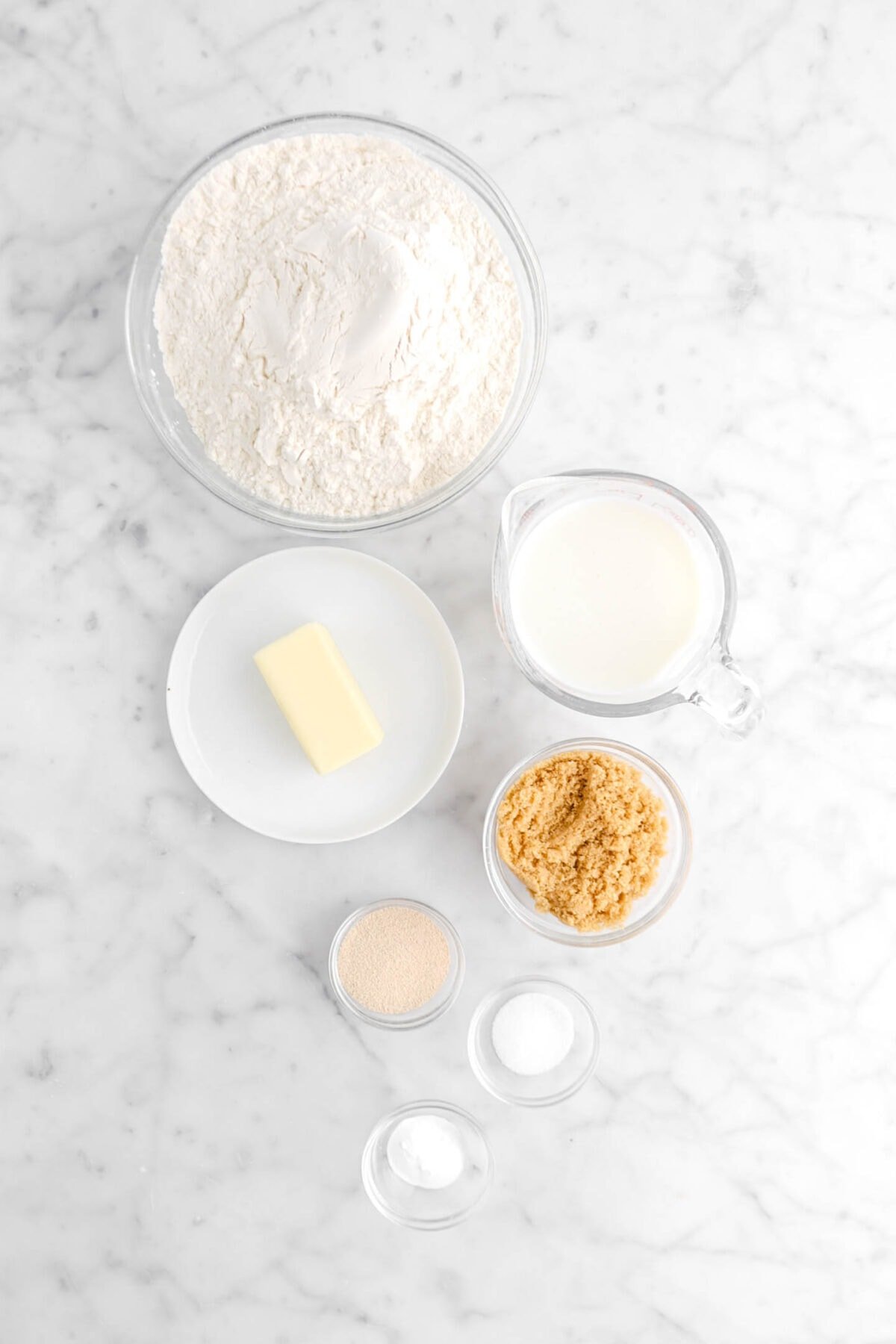 flour, butter, milk, brown sugar, yeast, salt, and baking powder on marble surface