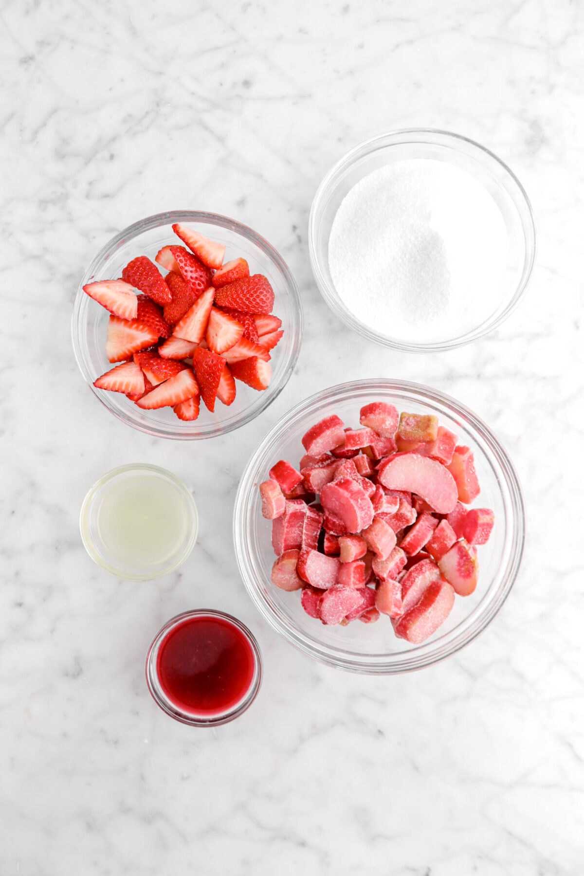 sugar, chopped strawberries, chopped rhubarb, lemon juice, and blood orange juice in glass bowls on marble surface