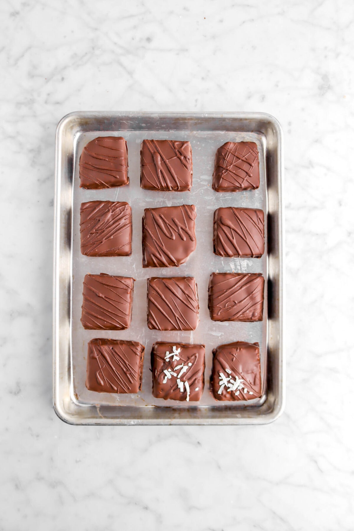 twelve square chocolates on small sheet pan with coconut flakes on two chocolates