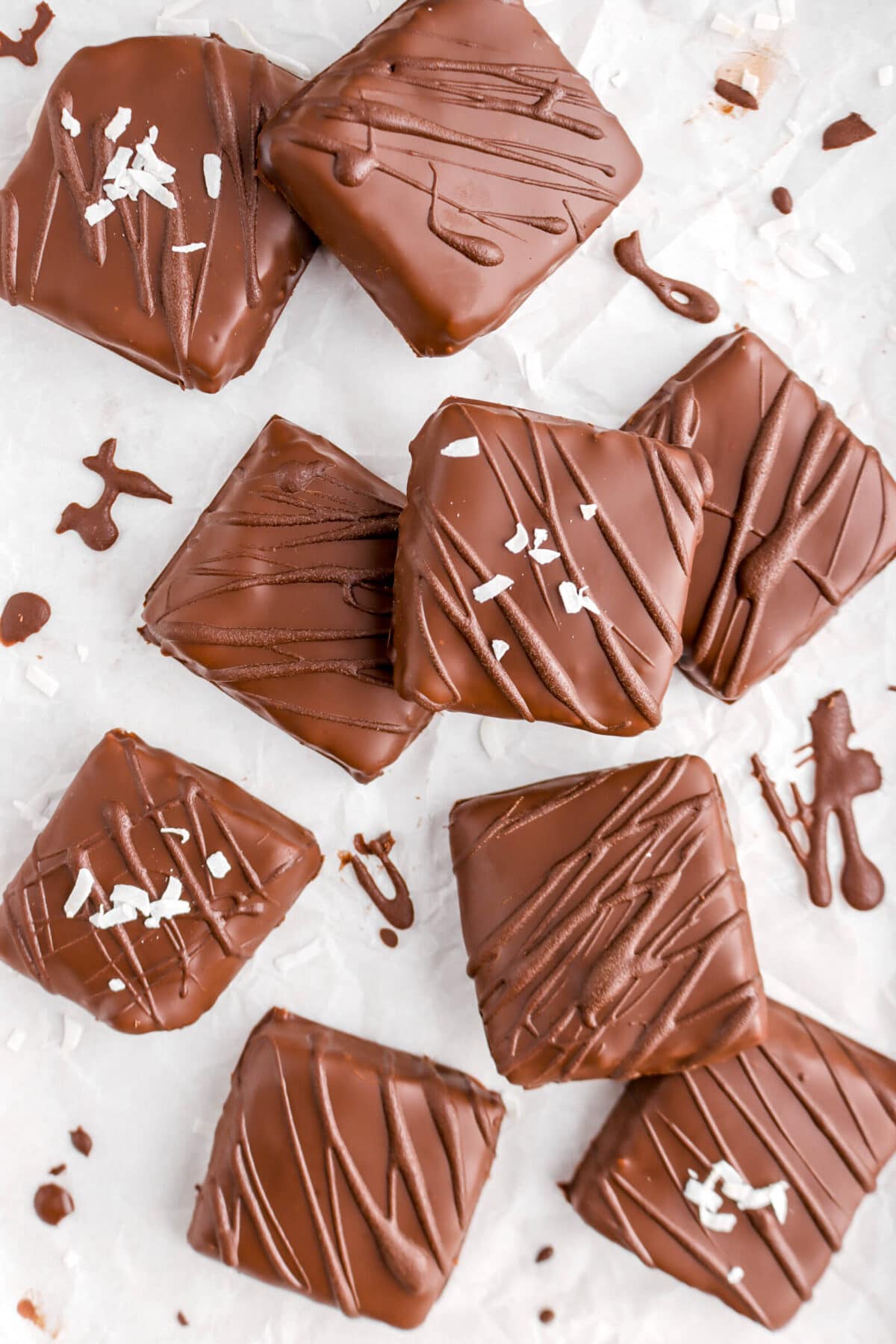 nine square chocolates on crinkled parchment paper with coconut flakes on four of them