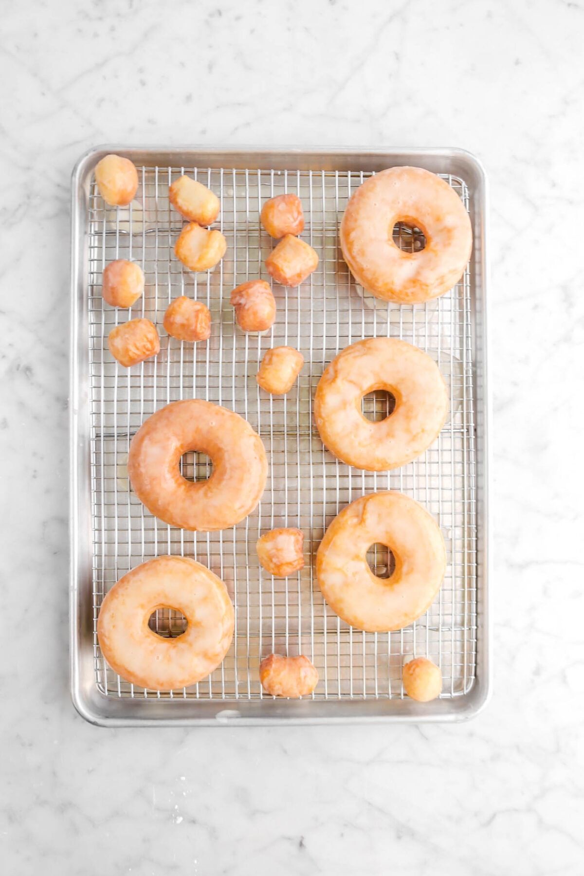 five glazed doughnuts on sheet pan with glazed doughnut holes
