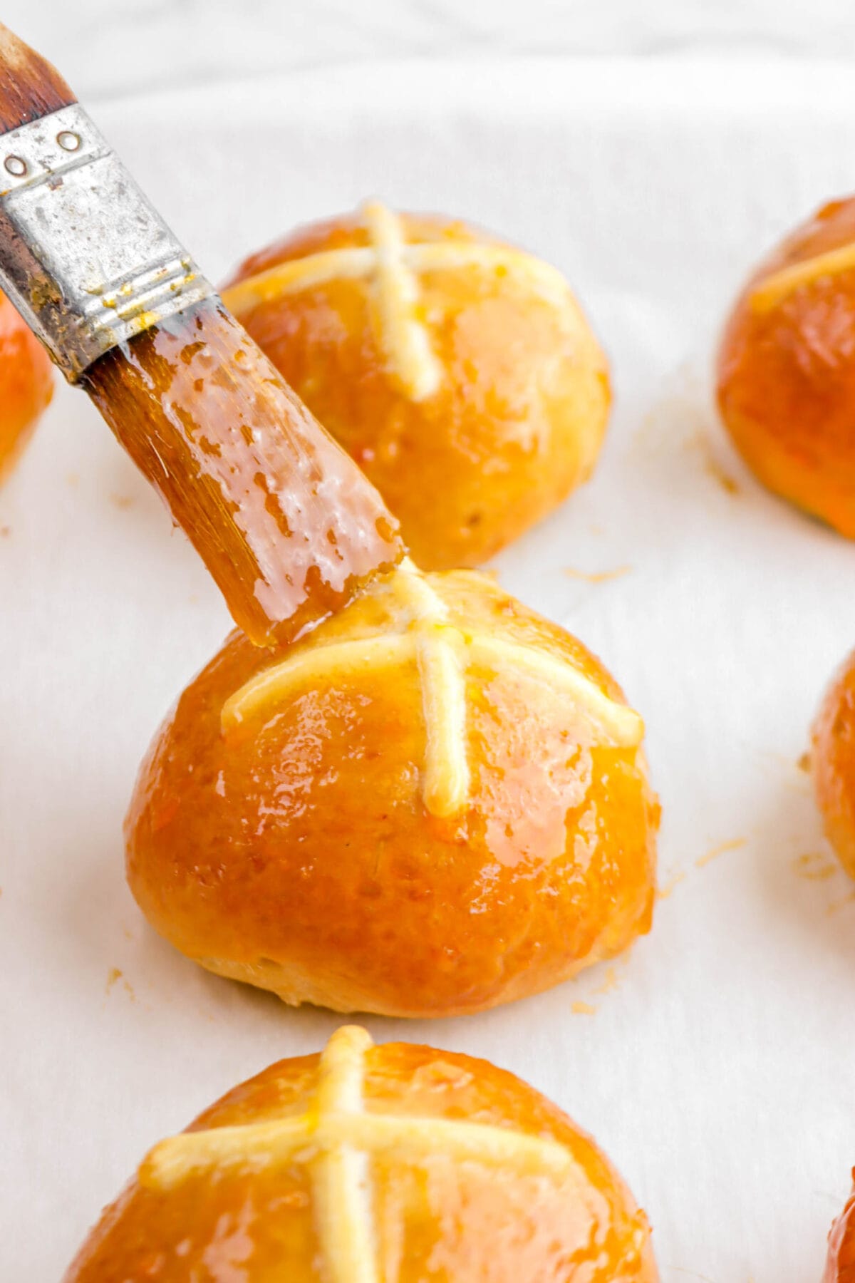 hot cross bun being brushed with apricot jam