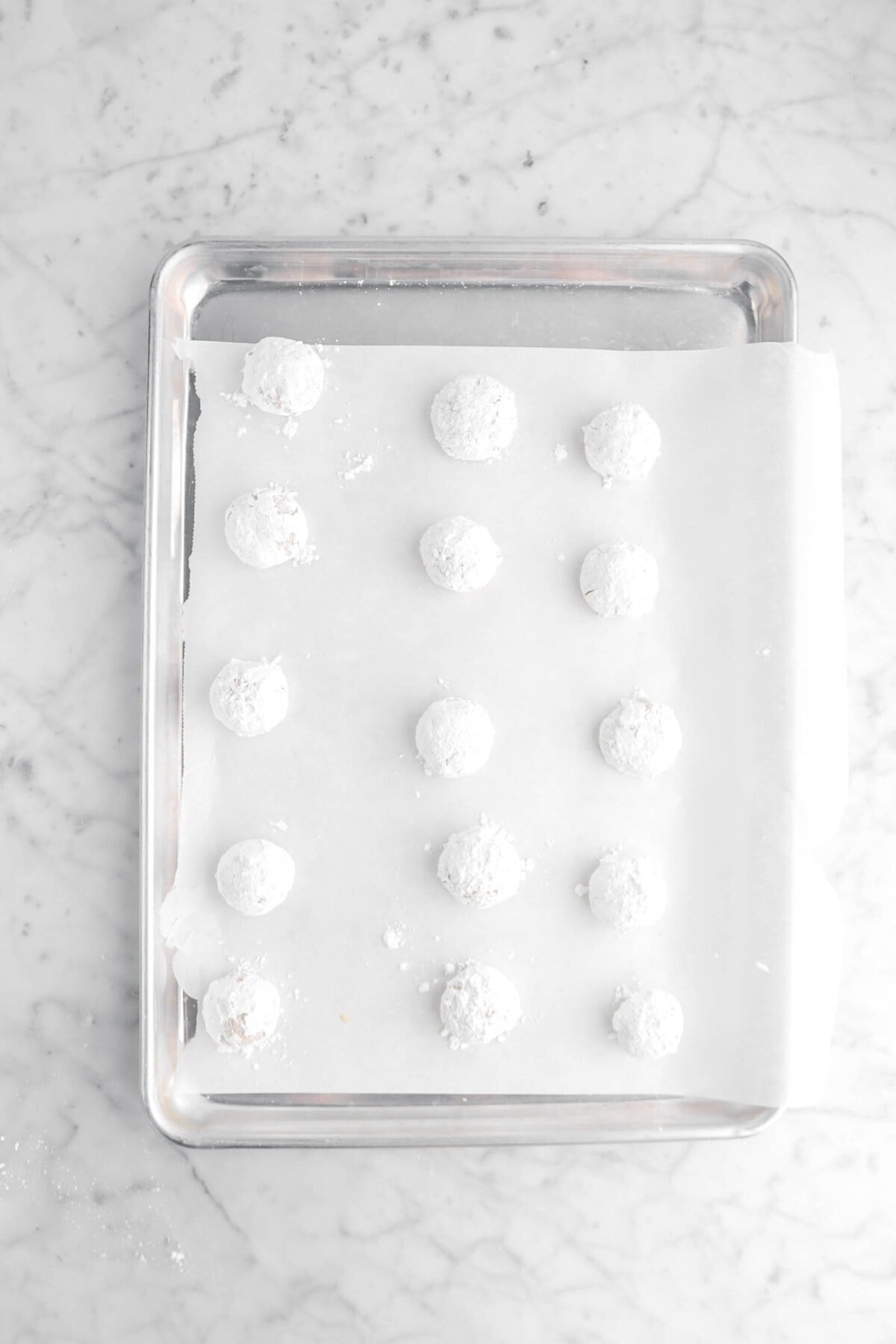 powdered sugar coated cookie dough balls on lined sheet pan
