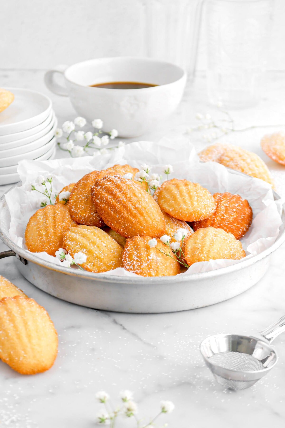 front shot of madeleines in pie pan with flowers and cup of coffee behind