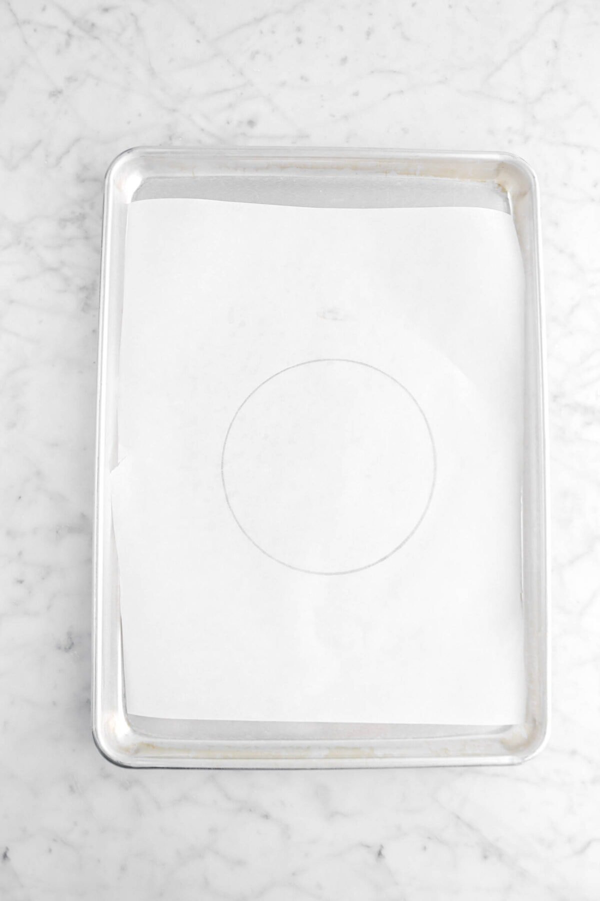 parchment paper with circle drawn on it lining a sheet pan on marle surface