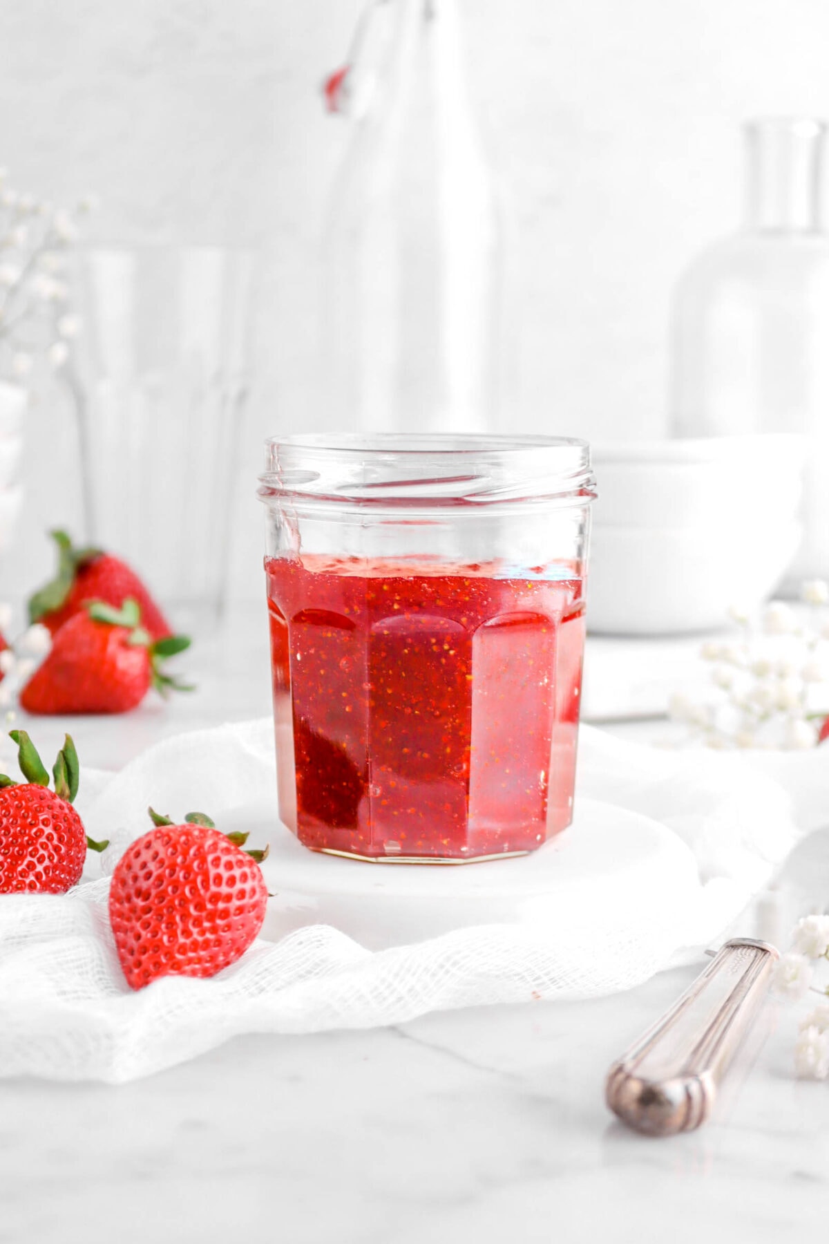 close up of jar of jam on upside down white plate with fresh strawberries beside
