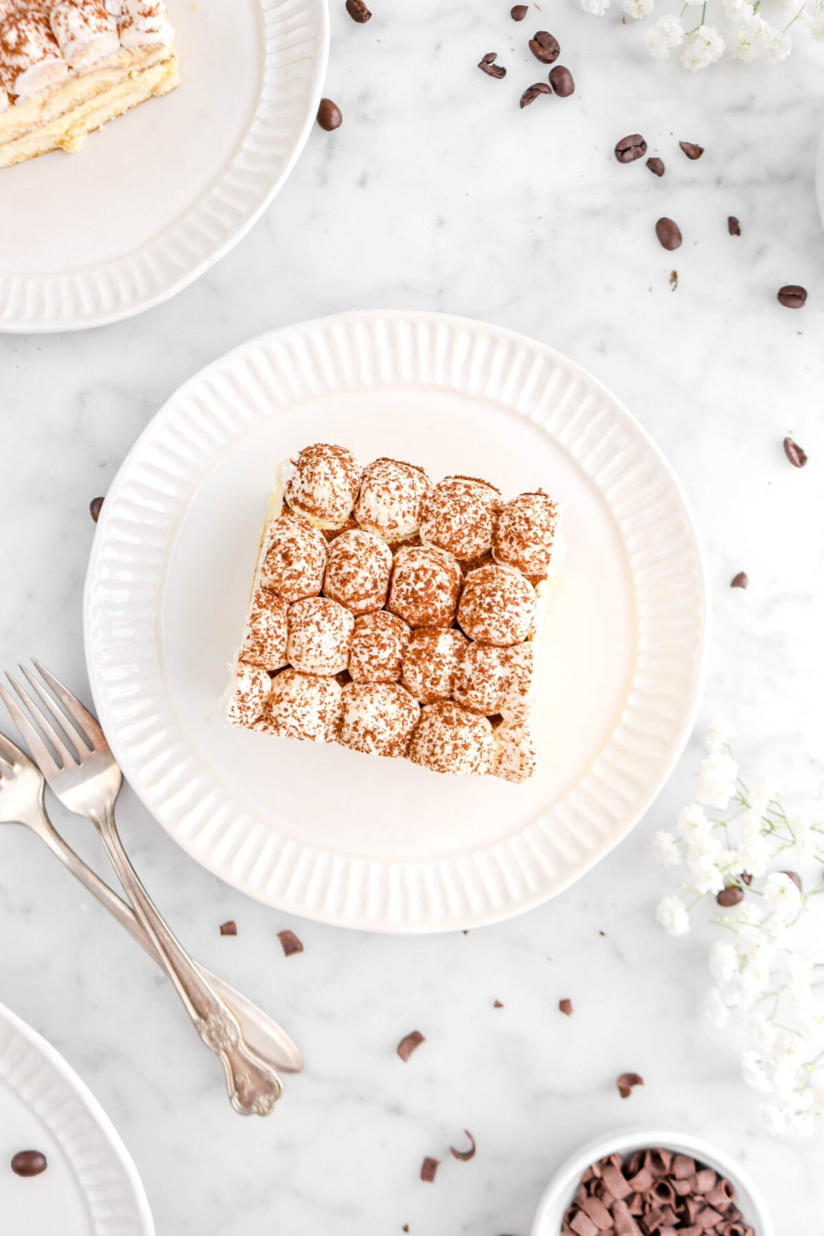 overhead shot of slice of tiramisu on white plate with two forks beside and coffee beans scattered around