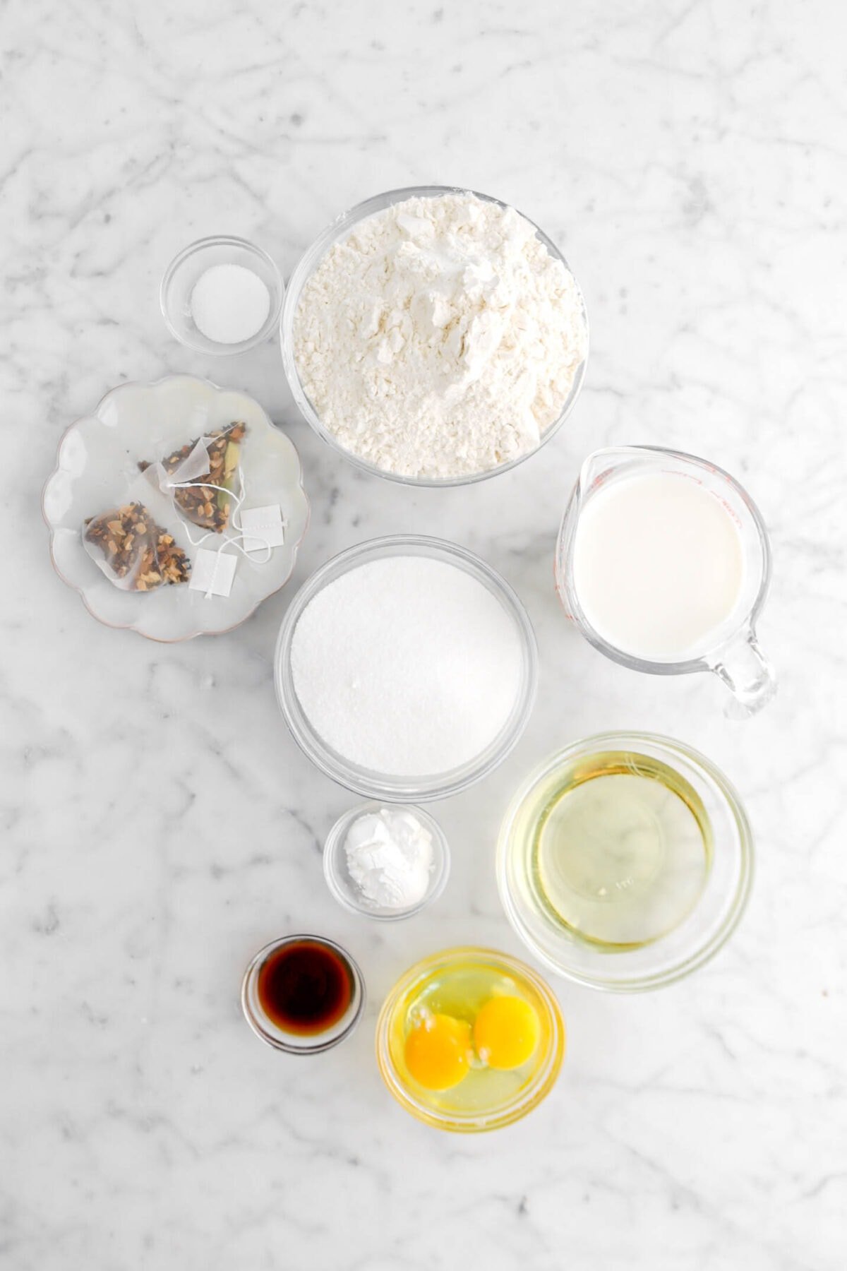 salt, flour, chai tea bags, sugar, milk, baking powder, vanilla, eggs, and oil on marble surface