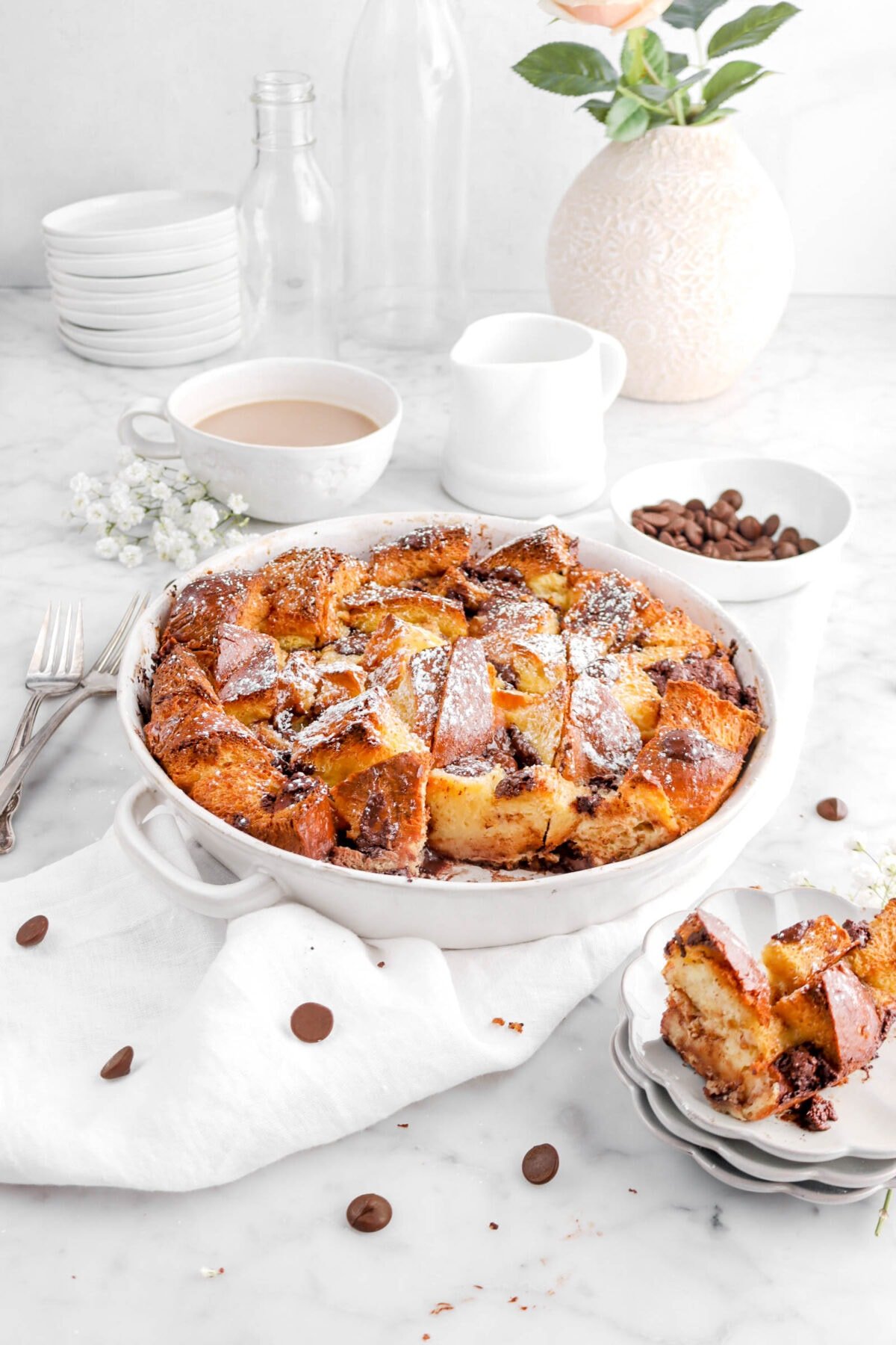 angled shot of bread pudding with slice missing, with chocolate chips and flowers around