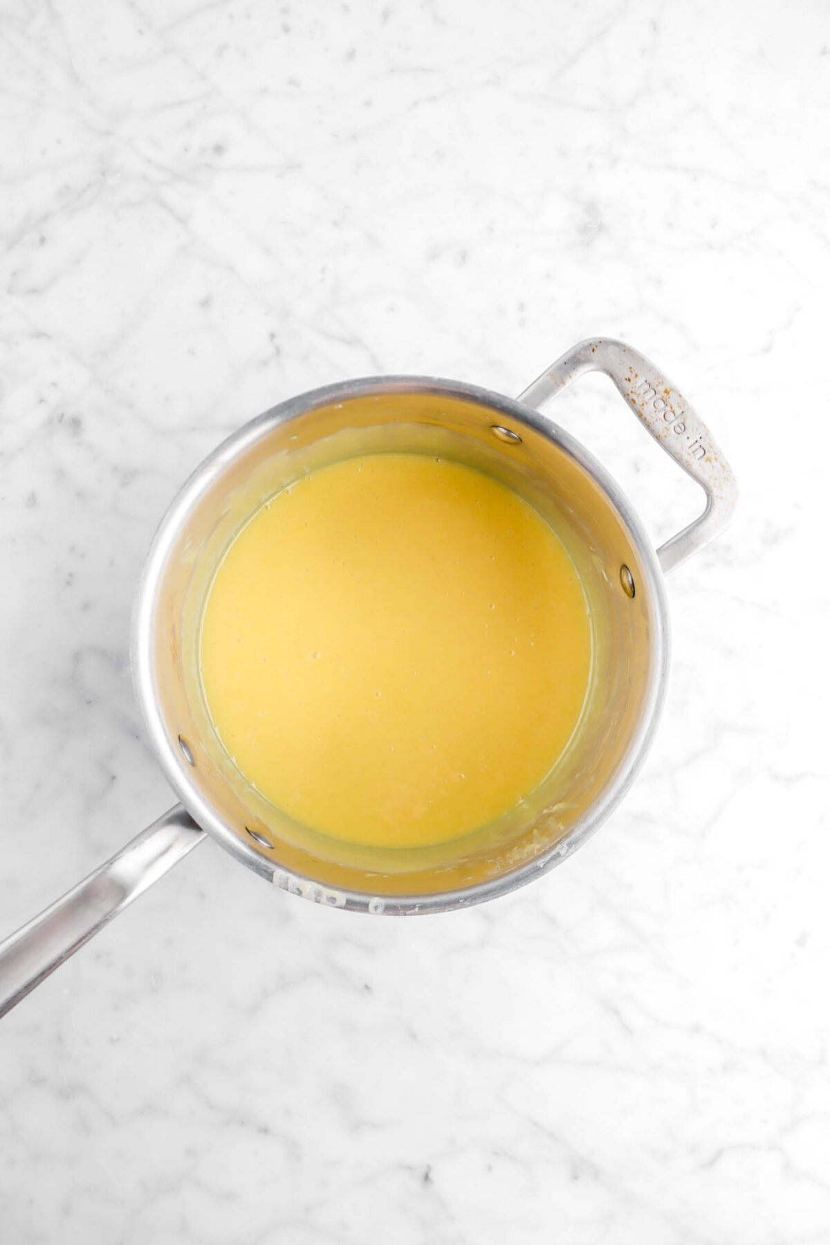 condensed milk and yolk mixture in large pot on marble surface