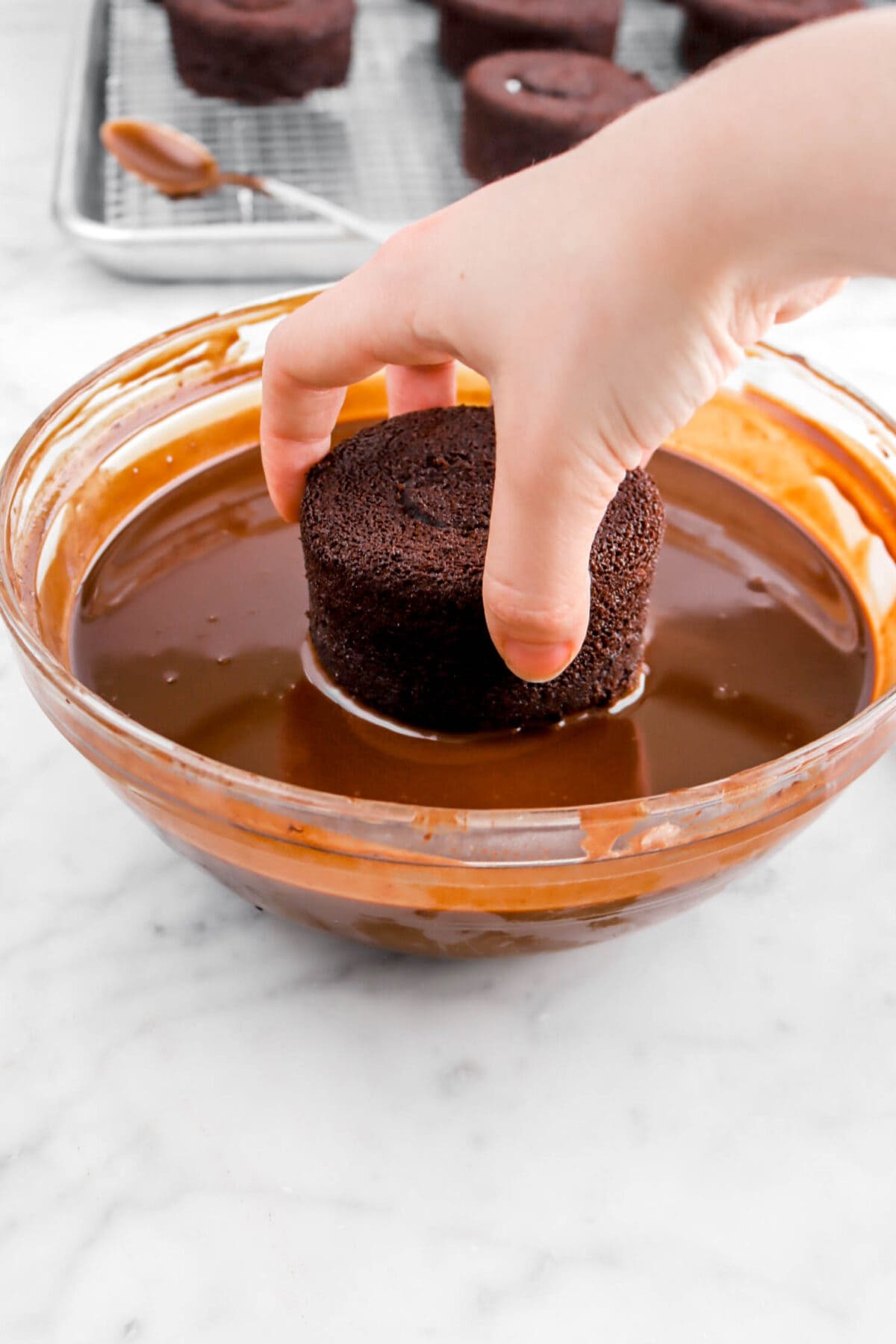 hand dipping mini chocolate cake in melted chocolate