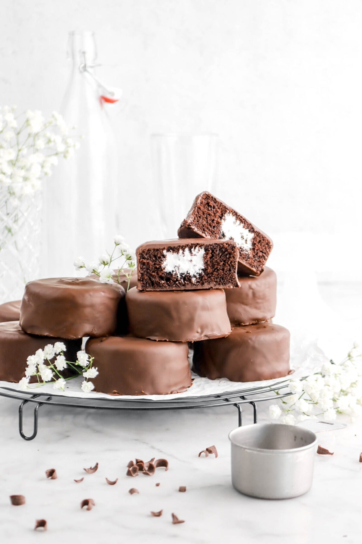 stacked mini chocolate coated chocolate cakes with one sliced in half, leaning against itself, with flowers around