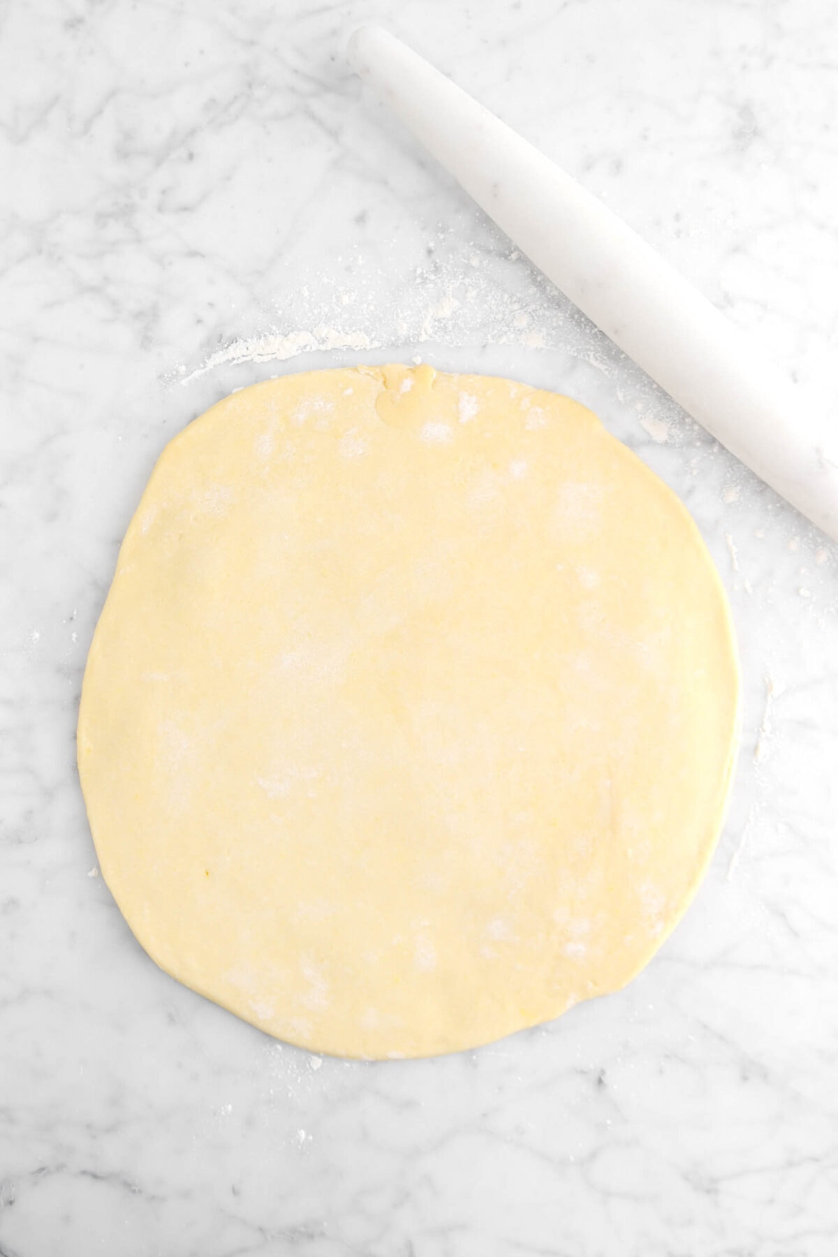 rolled out dough on marble surface with marble rolling pin beside