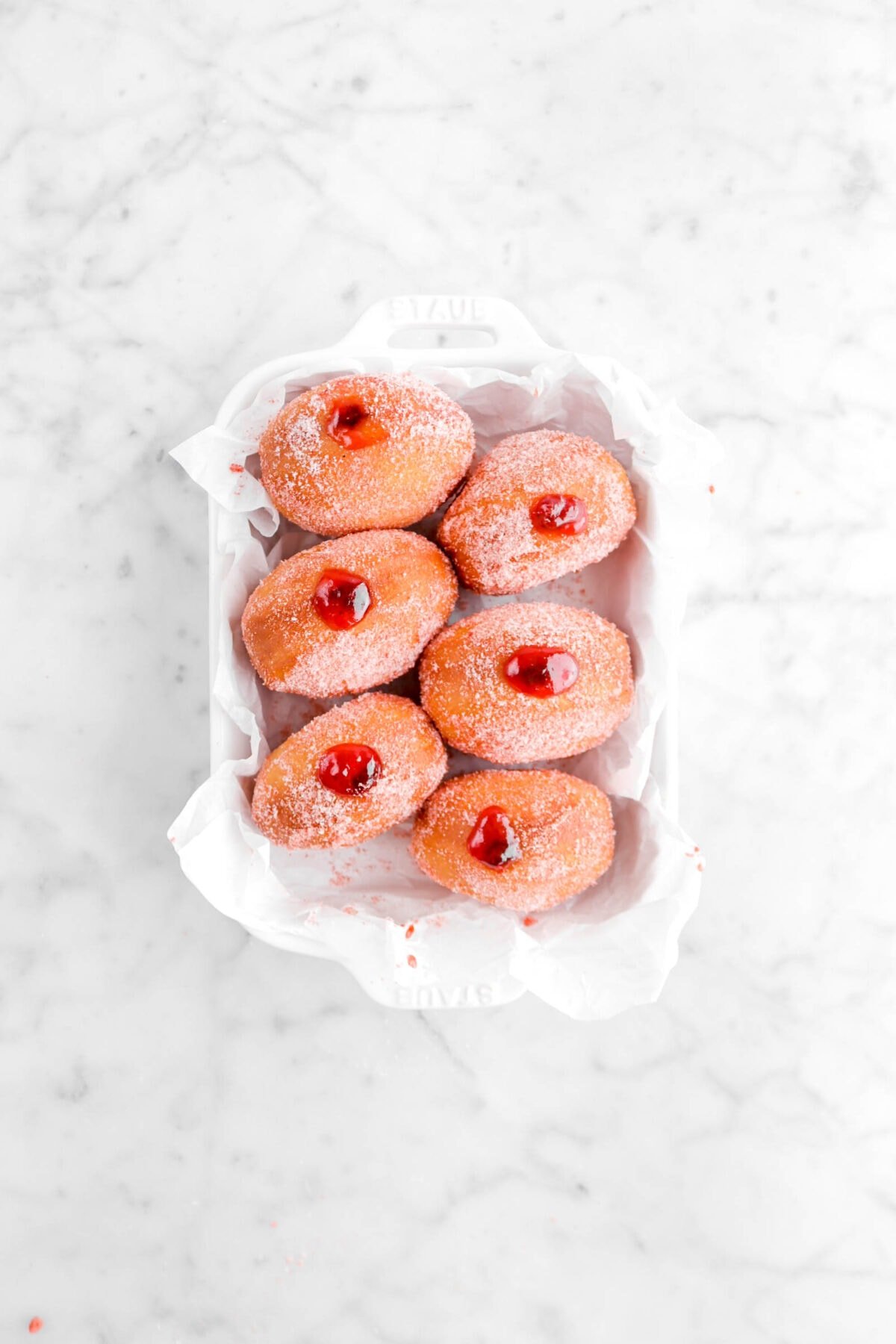six sugar coated doughnuts filled with jam in small white casserole