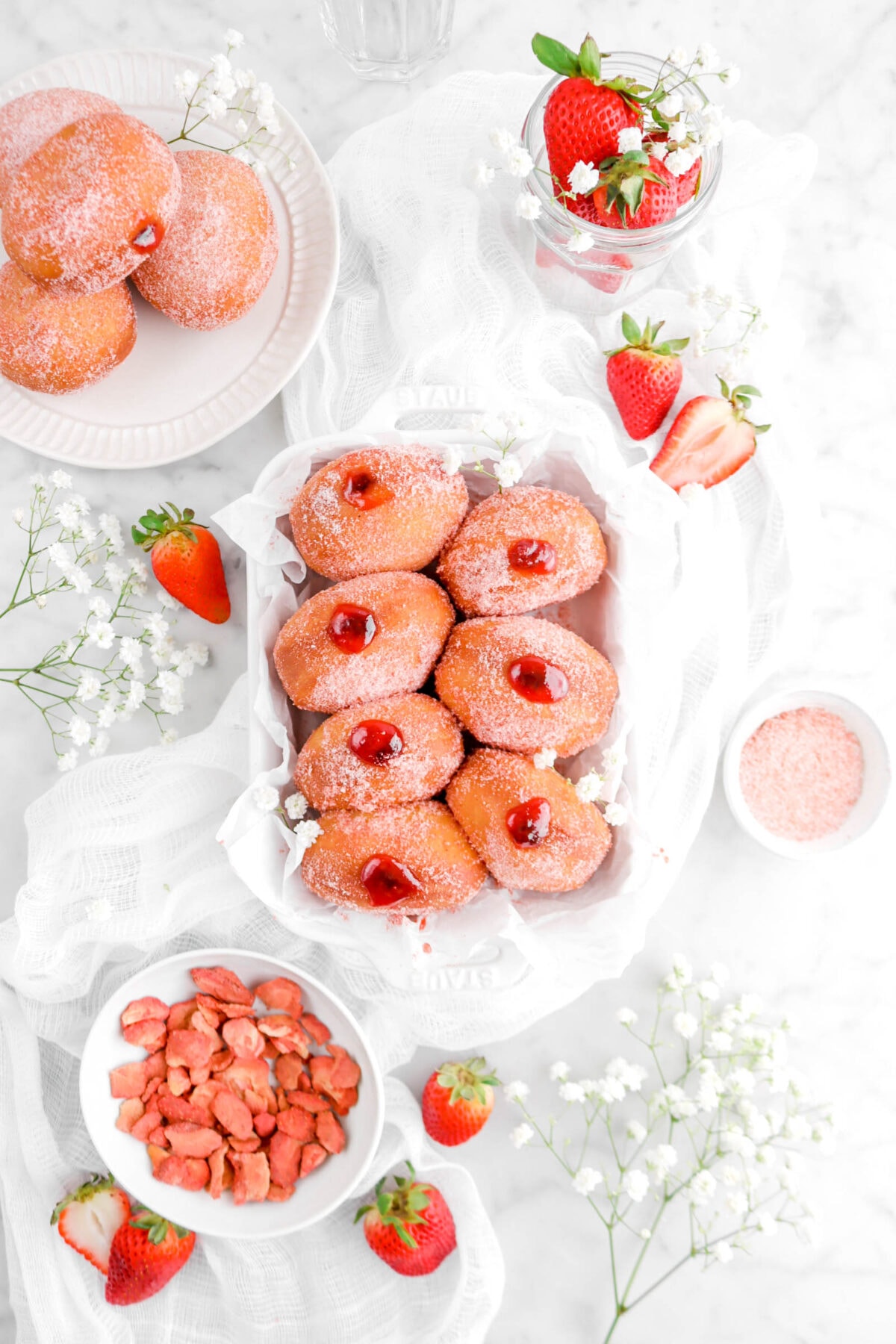 seven jam filled doughnuts in white casserole with flowers and strawberries around