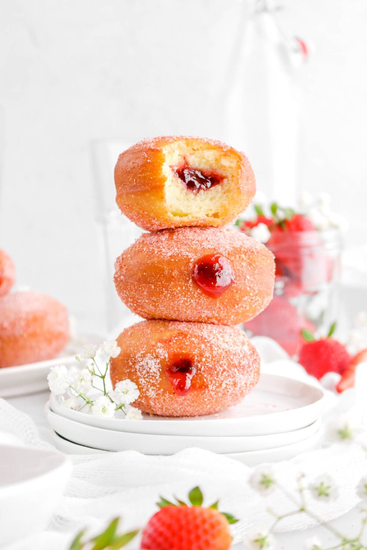 three stacked strawberry filled doughnuts with bite taken out of the one on top