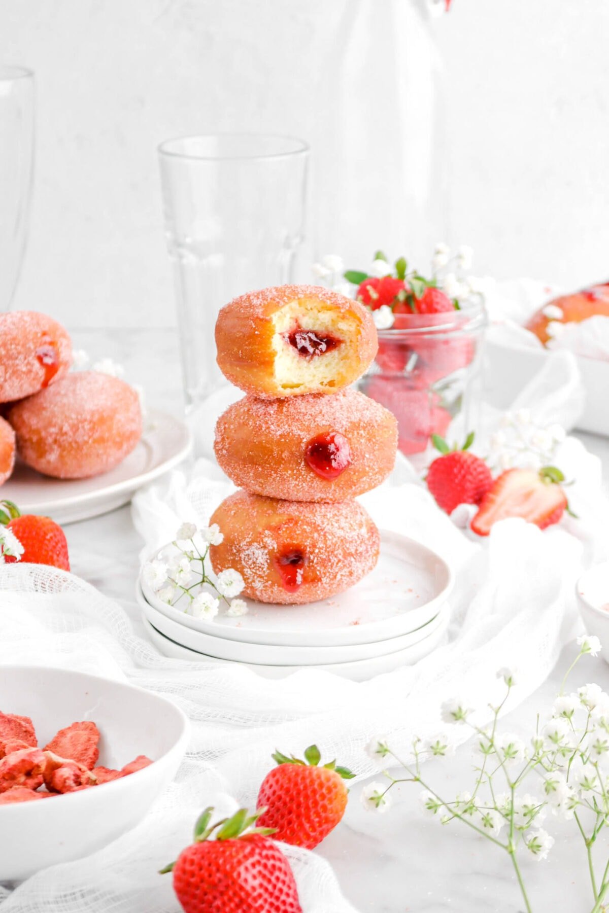 three stacked strawberry filled doughnuts on three stacked white plates with fresh strawberries and flowers around