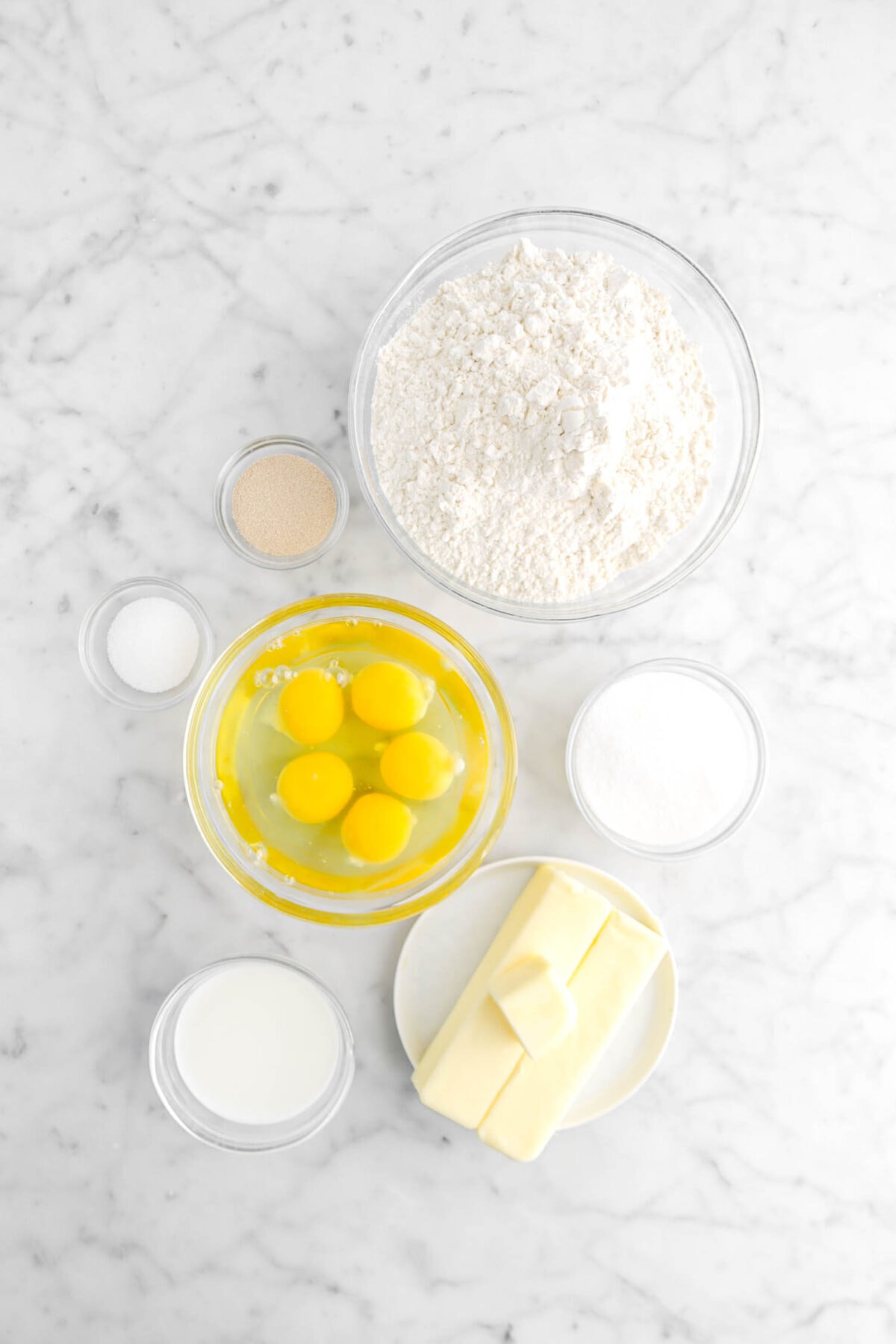 flour, yeast, salt, eggs, butter sugar, and milk on marble surface