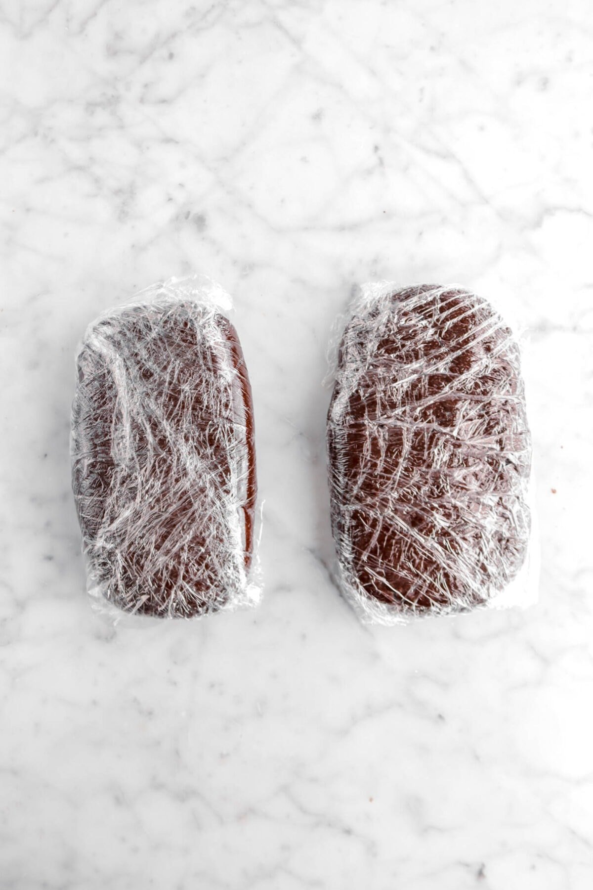 dough divided into two loaves wrapped in plastic wrap on marble surface