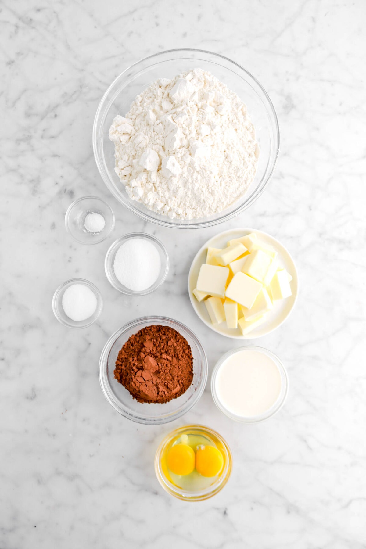 flour, baking powder, sugar, salt, cocoa powder, eggs, milk, and chopped butter on marble surface