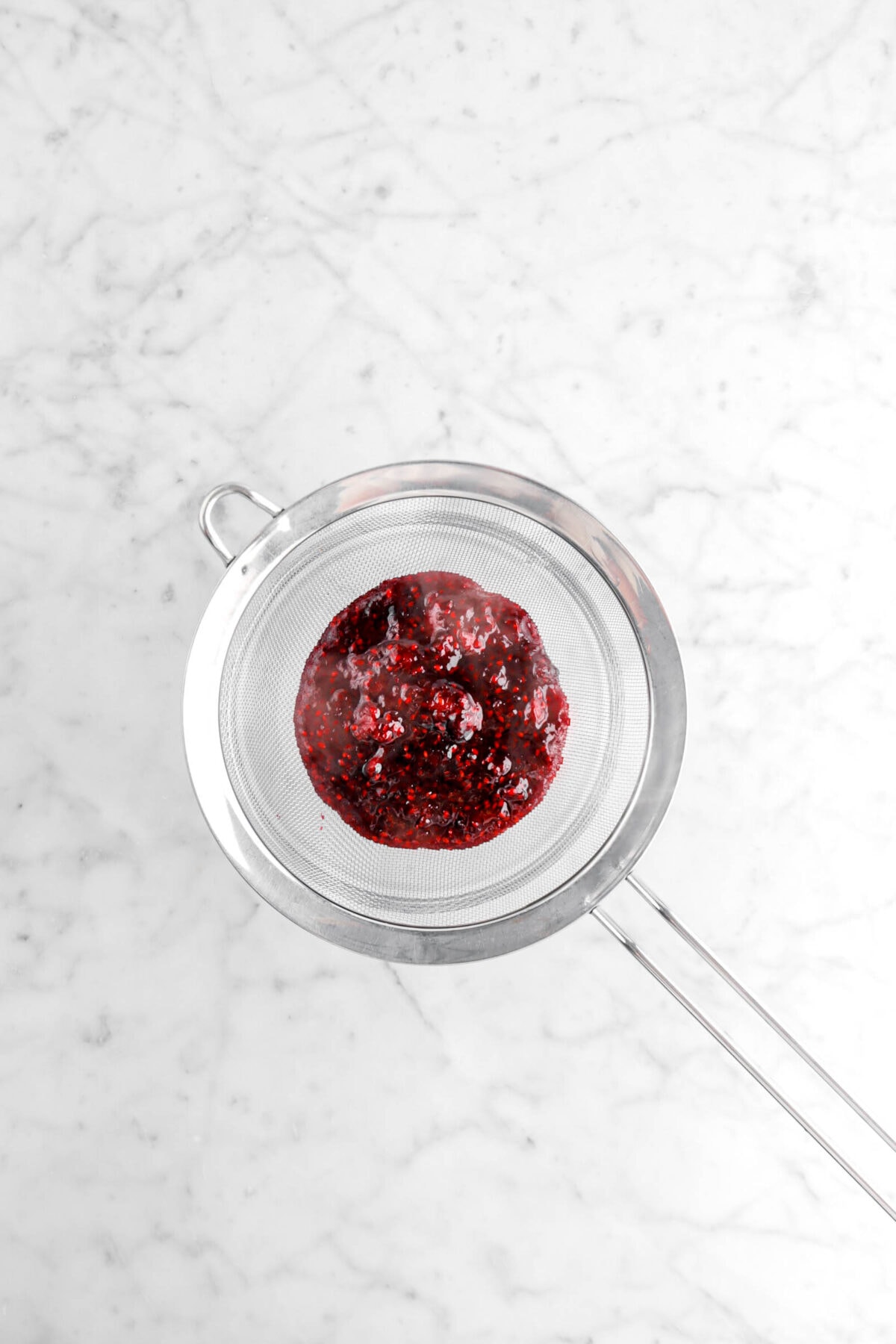 blackberry jam in sieve over glass bowl